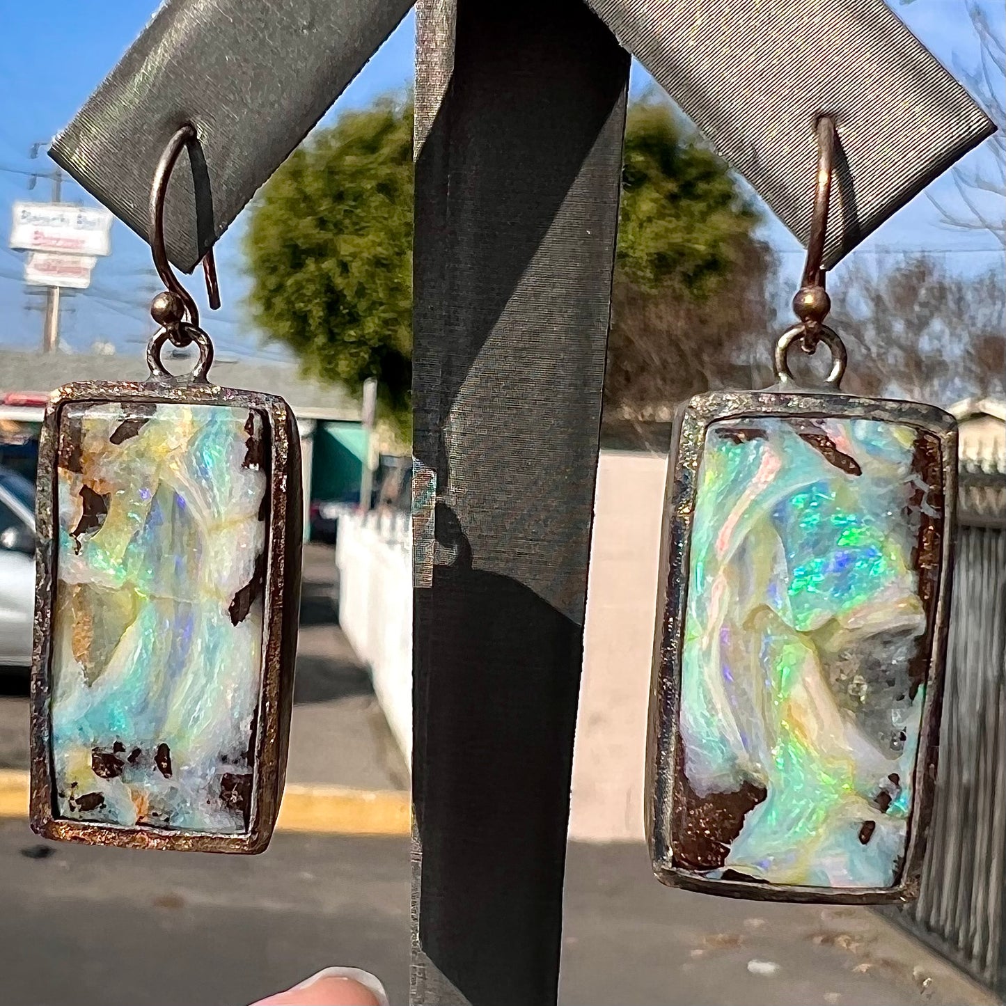 A pair of handmade sterling silver boulder opal earrings.  The earrings dangle from French wire hooks.