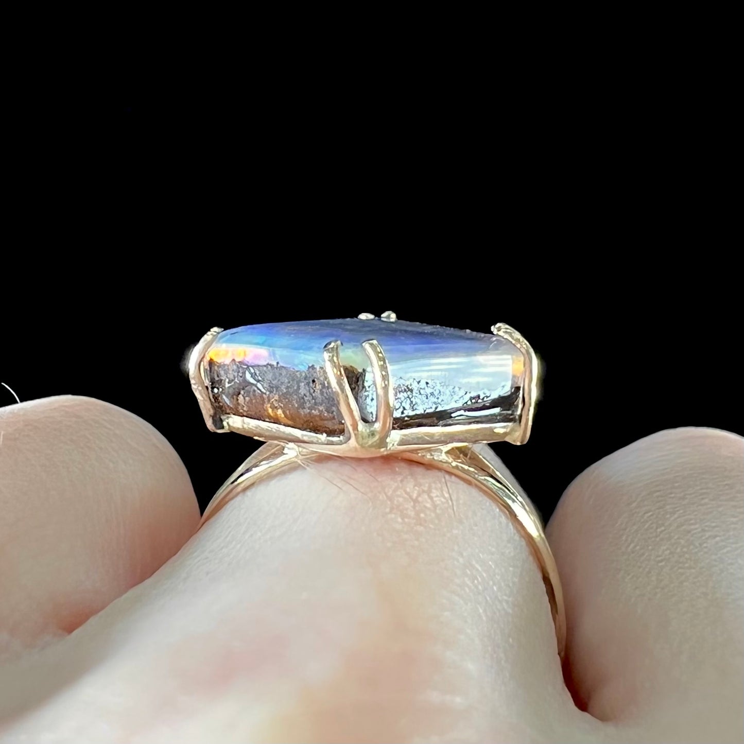 A ladies' boulder opal solitaire ring, handmade in yellow gold.  The stone is purple with flashes of blue, aqua, and green.