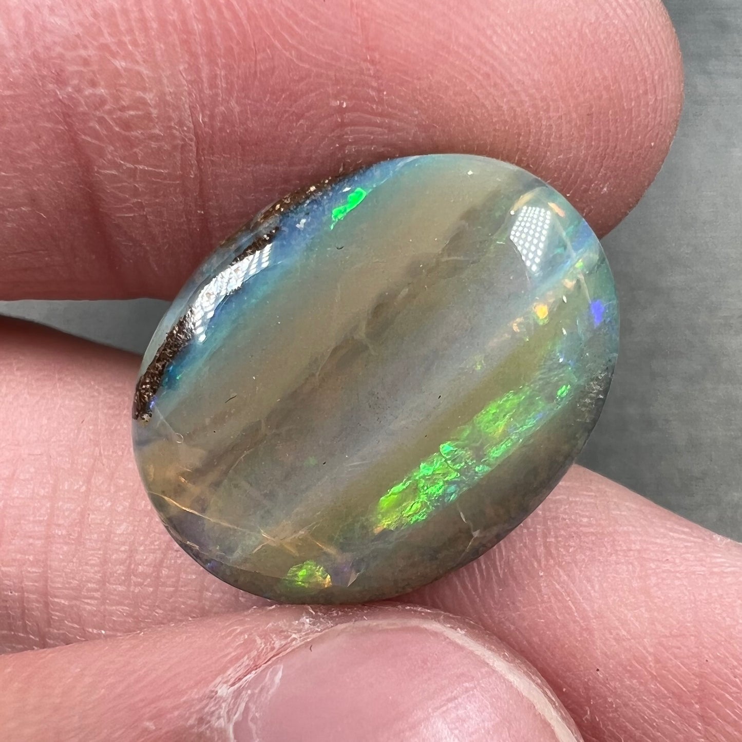 A loose, oval cabochon cut Quilpie boulder opal stone from Queensland, Australia.  The predominant color flash is green.