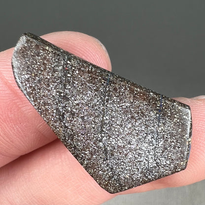 A loose, polished, freeform cut boulder opal stone from Queensland, Australia.