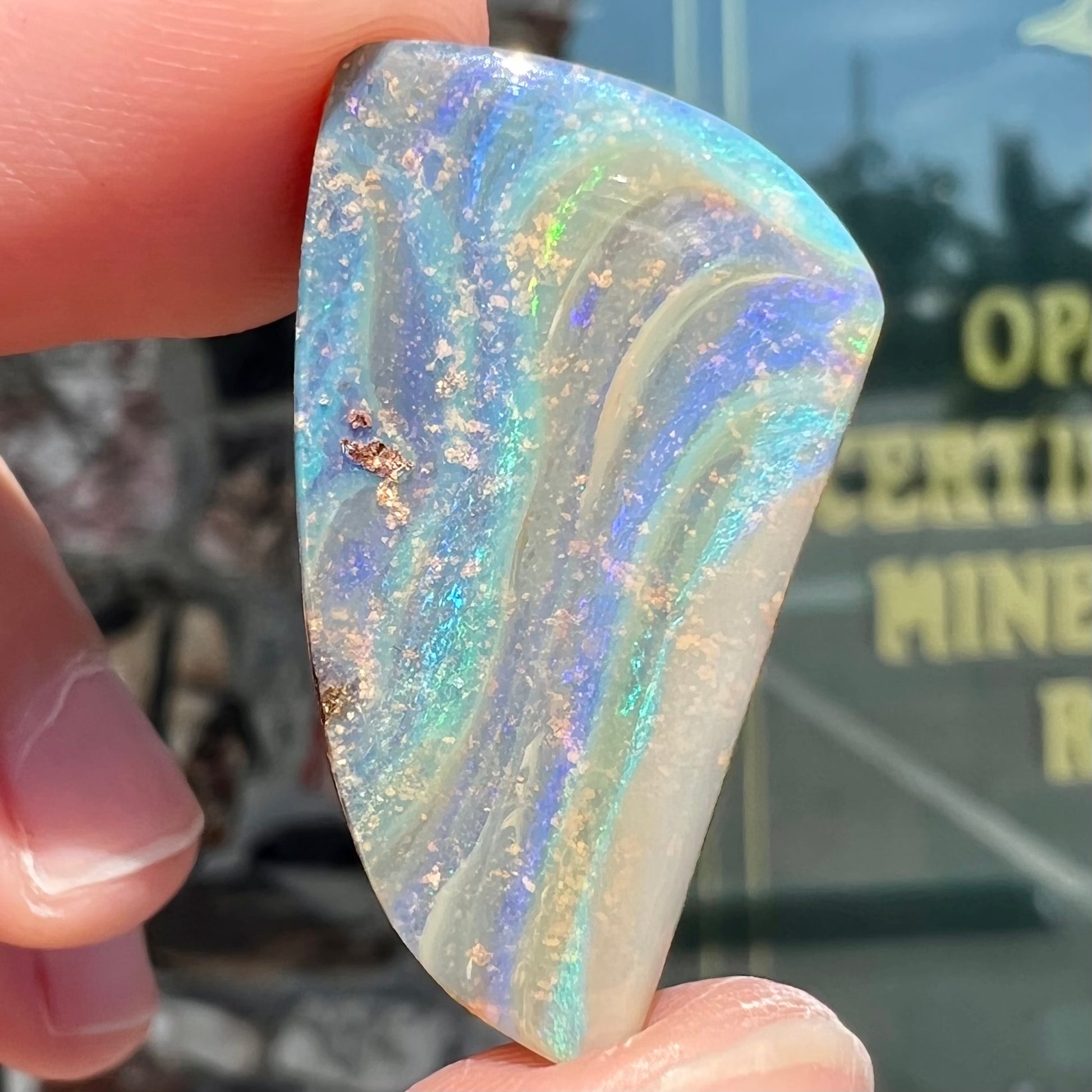 A polished, freeform shaped boulder opal stone from Queensland, Australia.  Predominant colors are green, blue, and violet.