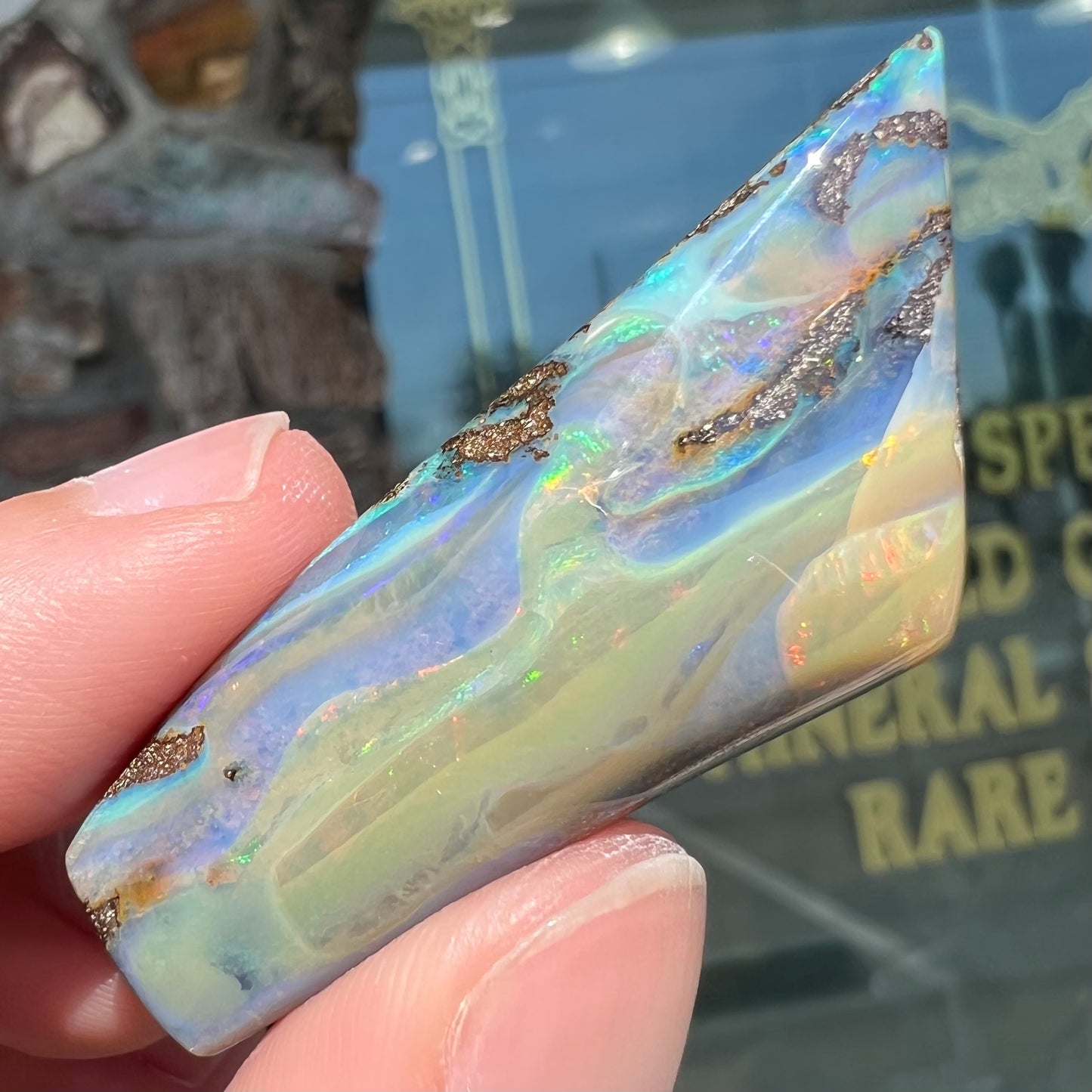 A freeform shaped, polished boulder opal stone from Queensland, Australia.  The stone has red, orange, green, and blue fire.
