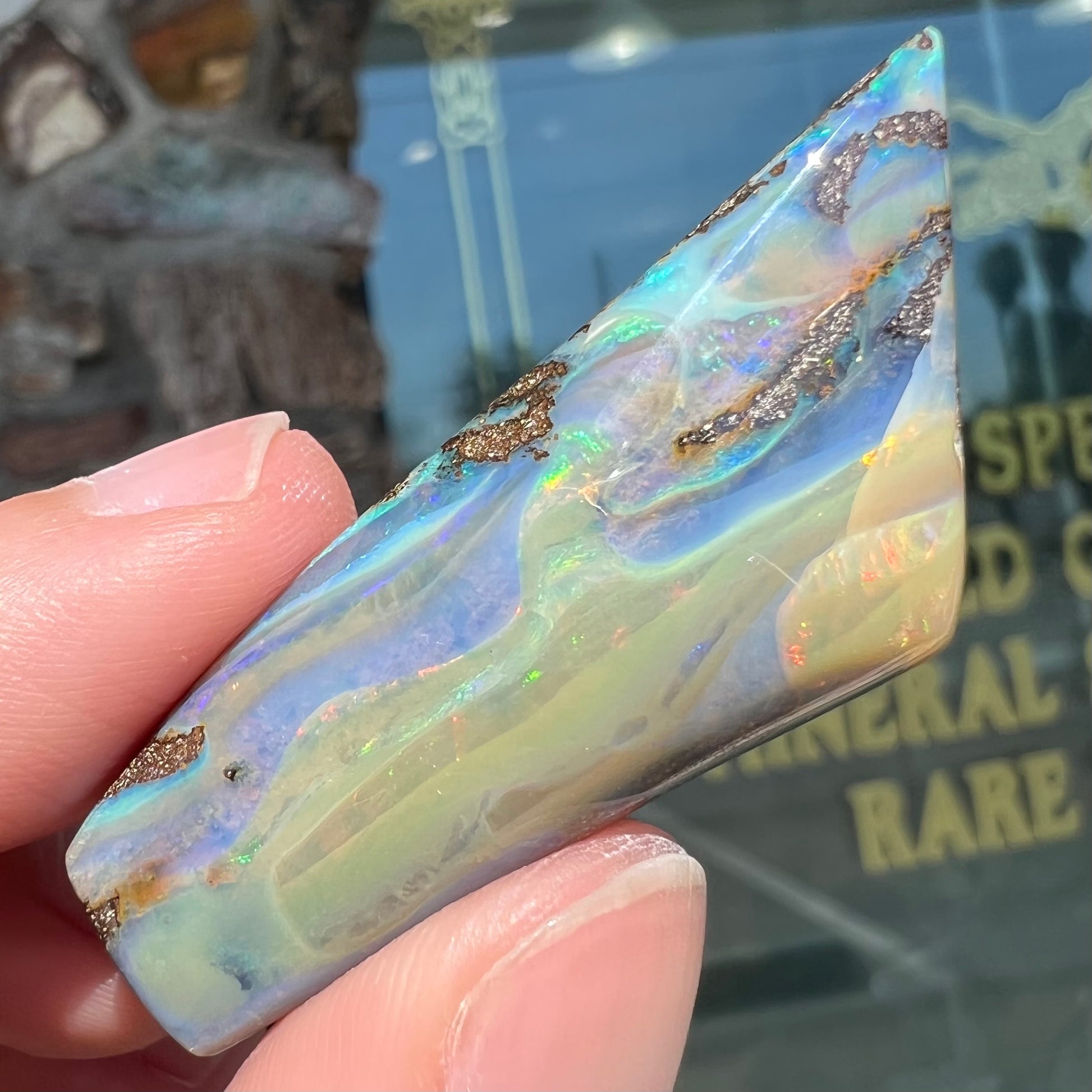 A freeform shaped, polished boulder opal stone from Queensland, Australia.  The stone has red, orange, green, and blue fire.