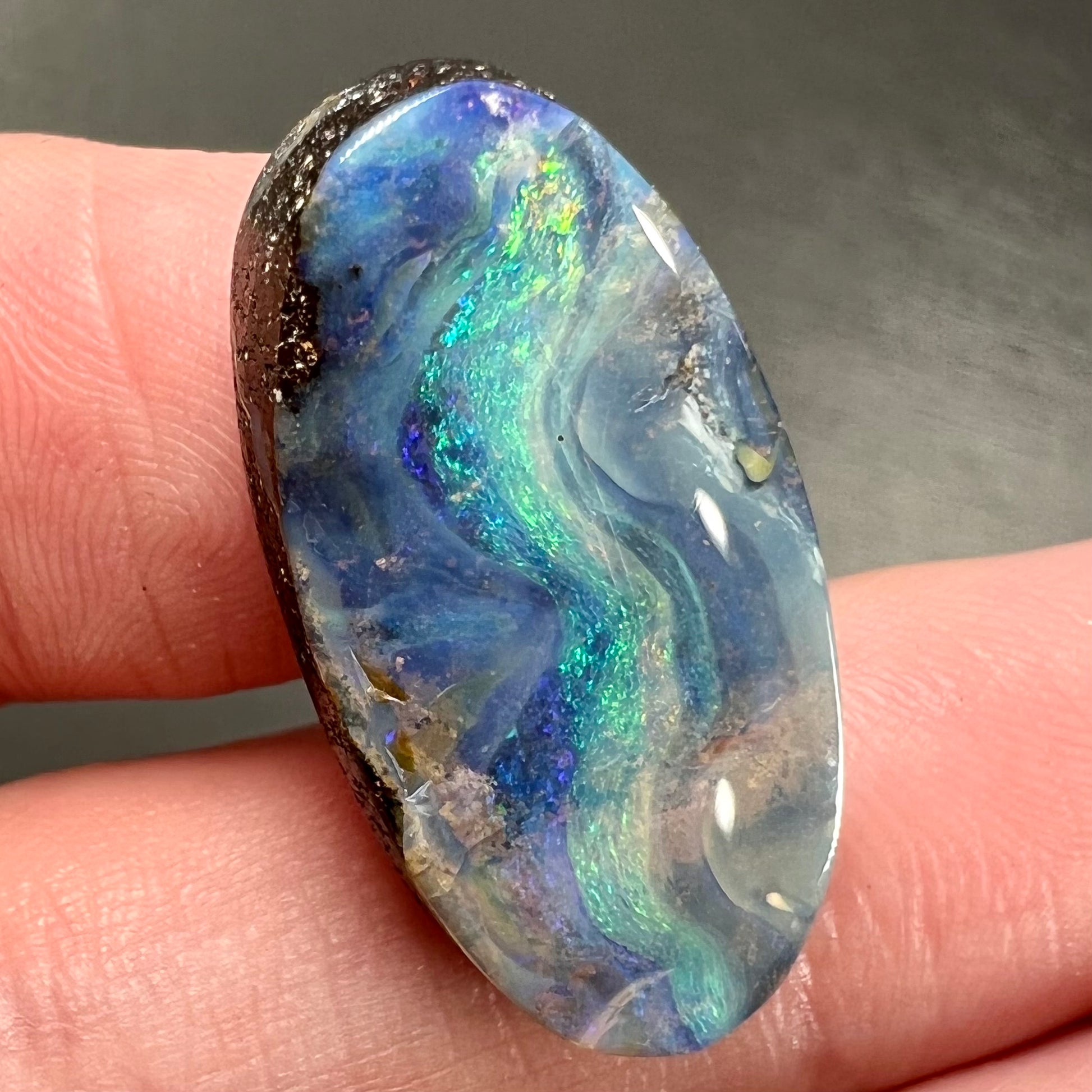 A loose, oval cabochon cut Quilpie boulder opal from Queensland, Australia.  The stone is blue with green fire.