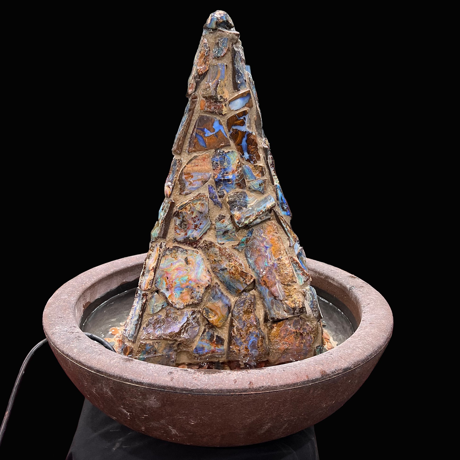 An indoor/outdoor three sided pyramid fountain made from Australian boulder opal, sitting in a bowl of Mexican fire opal.