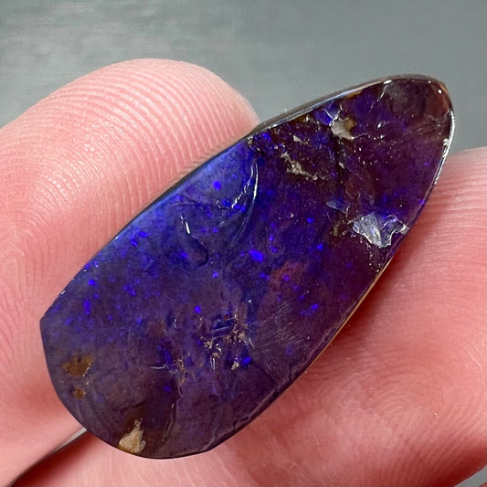 A loose, teardrop shaped purple boulder opal stone.