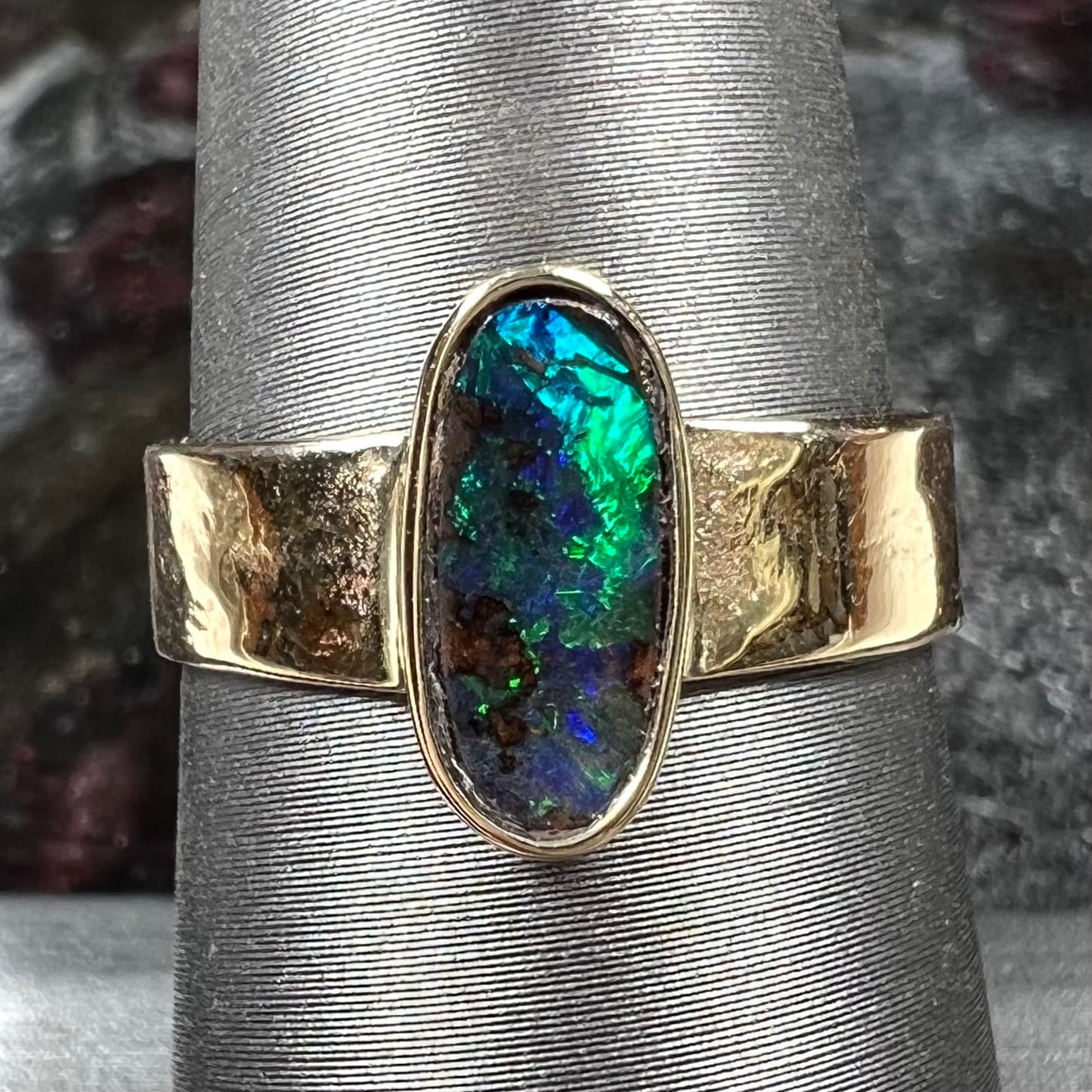 A blue green oval cabochon cut Australian boulder opal set in a yellow gold solitaire ring.