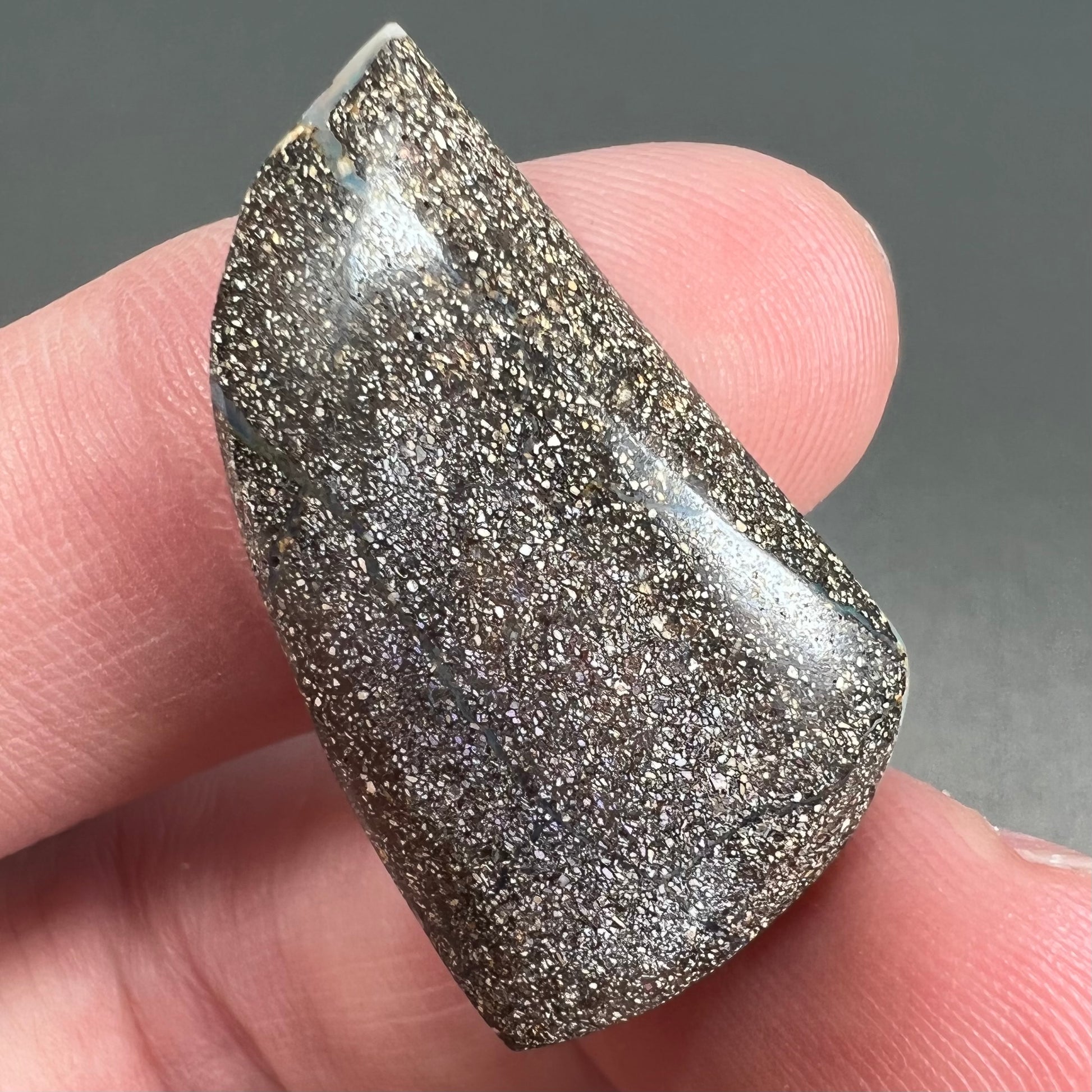 A polished, freeform shaped boulder opal stone from Queensland, Australia.  Predominant colors are green, blue, and violet.