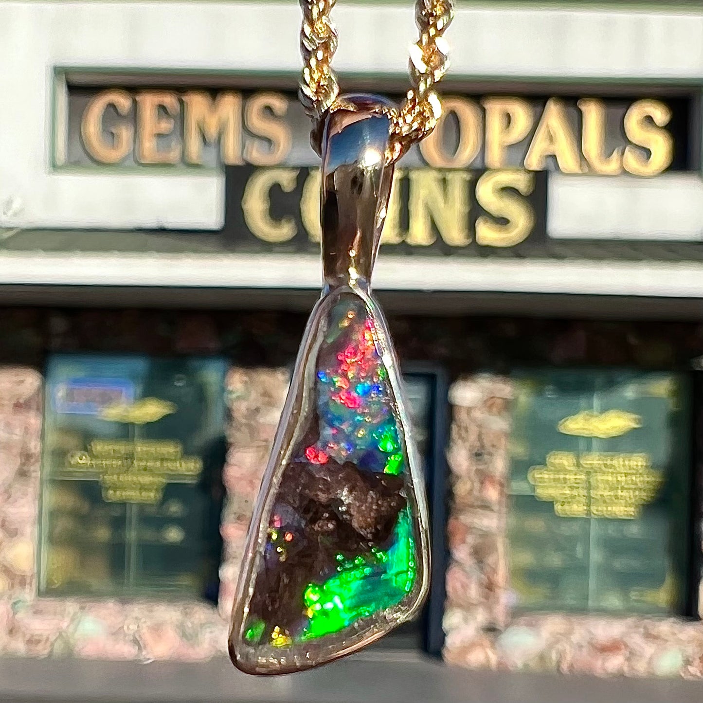 A bright green and red boulder opal bezel pendant in solid yellow gold.