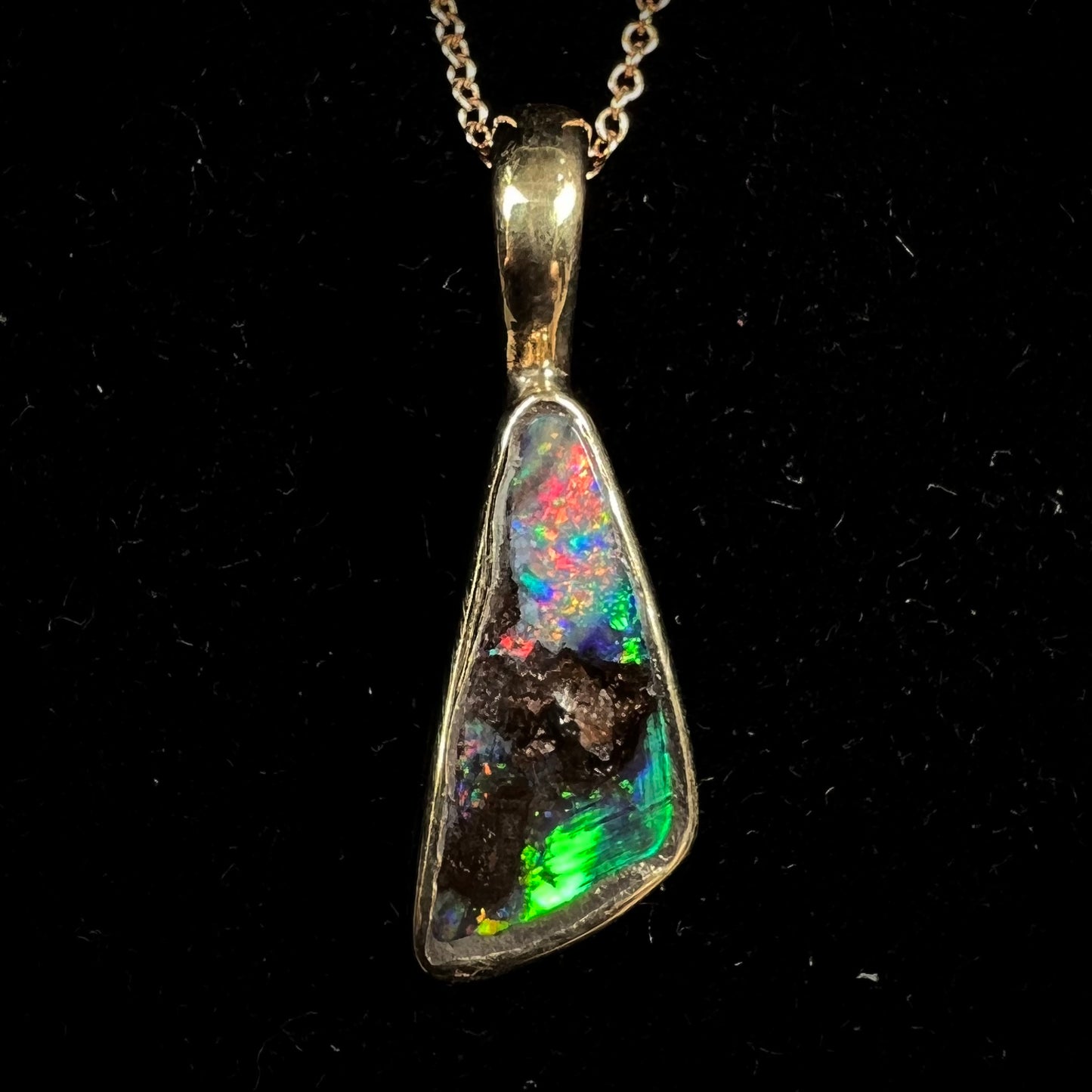 A bright green and red boulder opal bezel pendant in solid yellow gold.