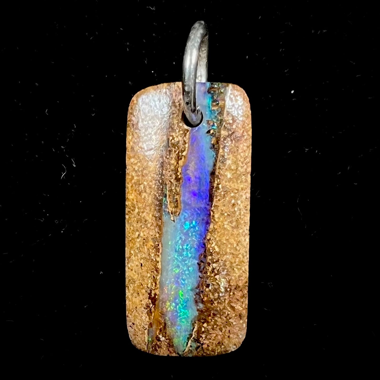 A drilled boulder opal stone with a sterling silver ring through the hole to be worn as a pendant.