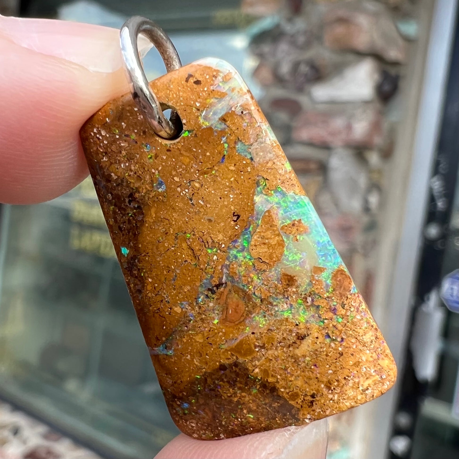 A drilled boulder opal stone with a sterling silver ring through the hole to be worn as a pendant.