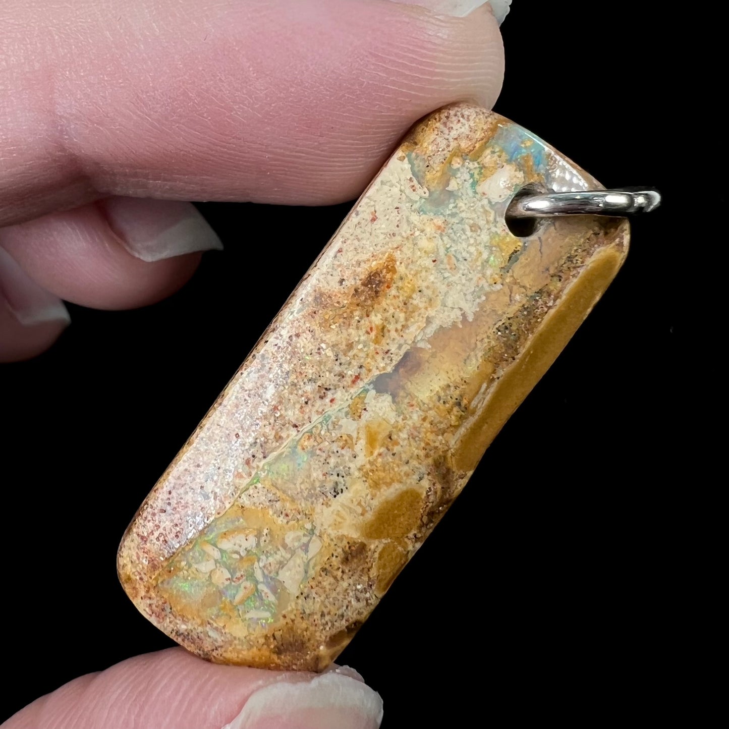 A drilled boulder opal stone with a sterling silver ring through the hole to be worn as a pendant.