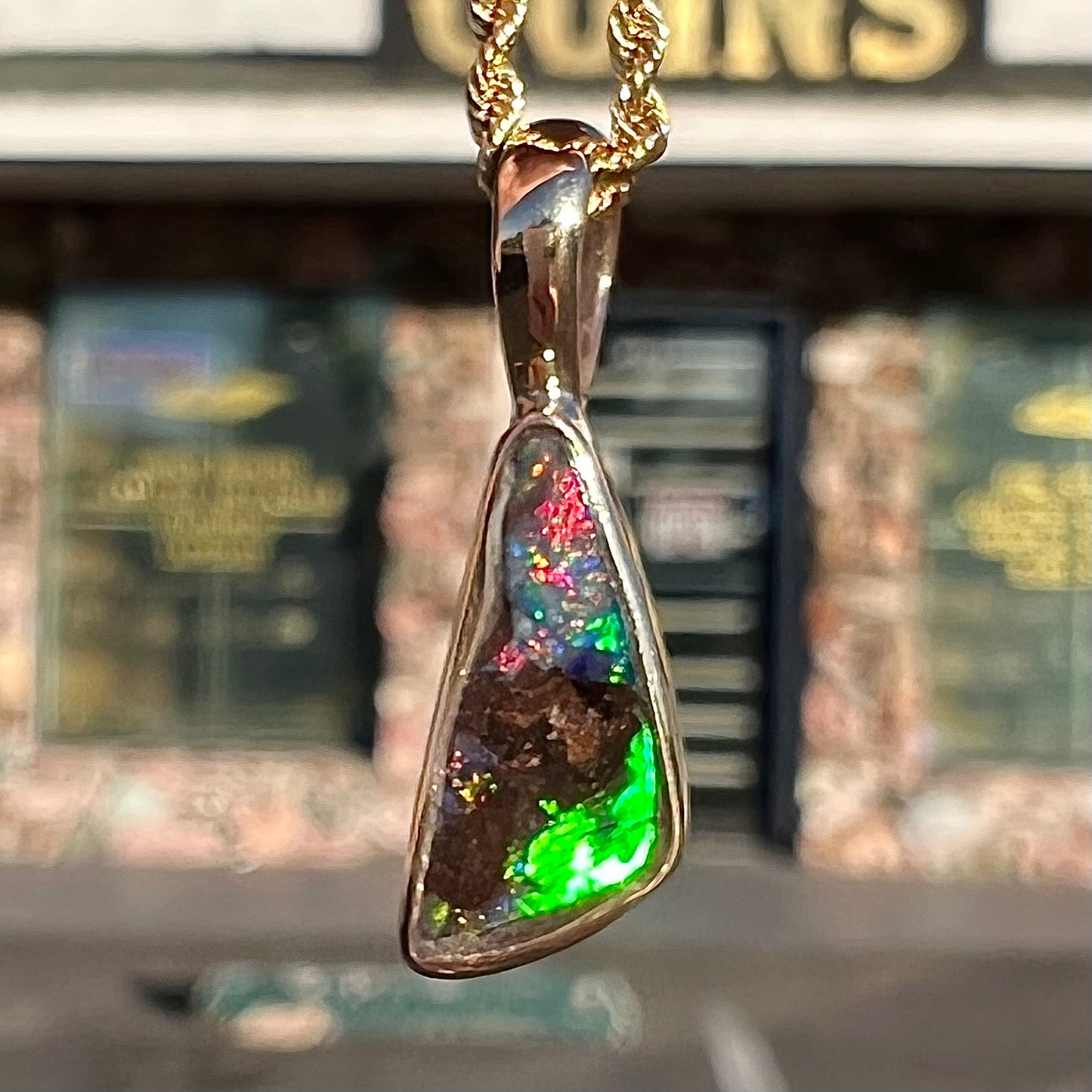 A bright green and red boulder opal bezel pendant in solid yellow gold.