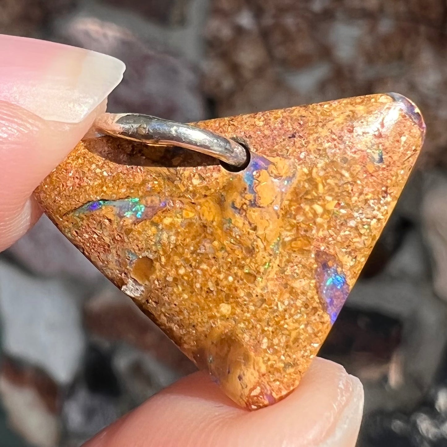 A drilled boulder opal stone with a sterling silver ring through the hole to be worn as a pendant.