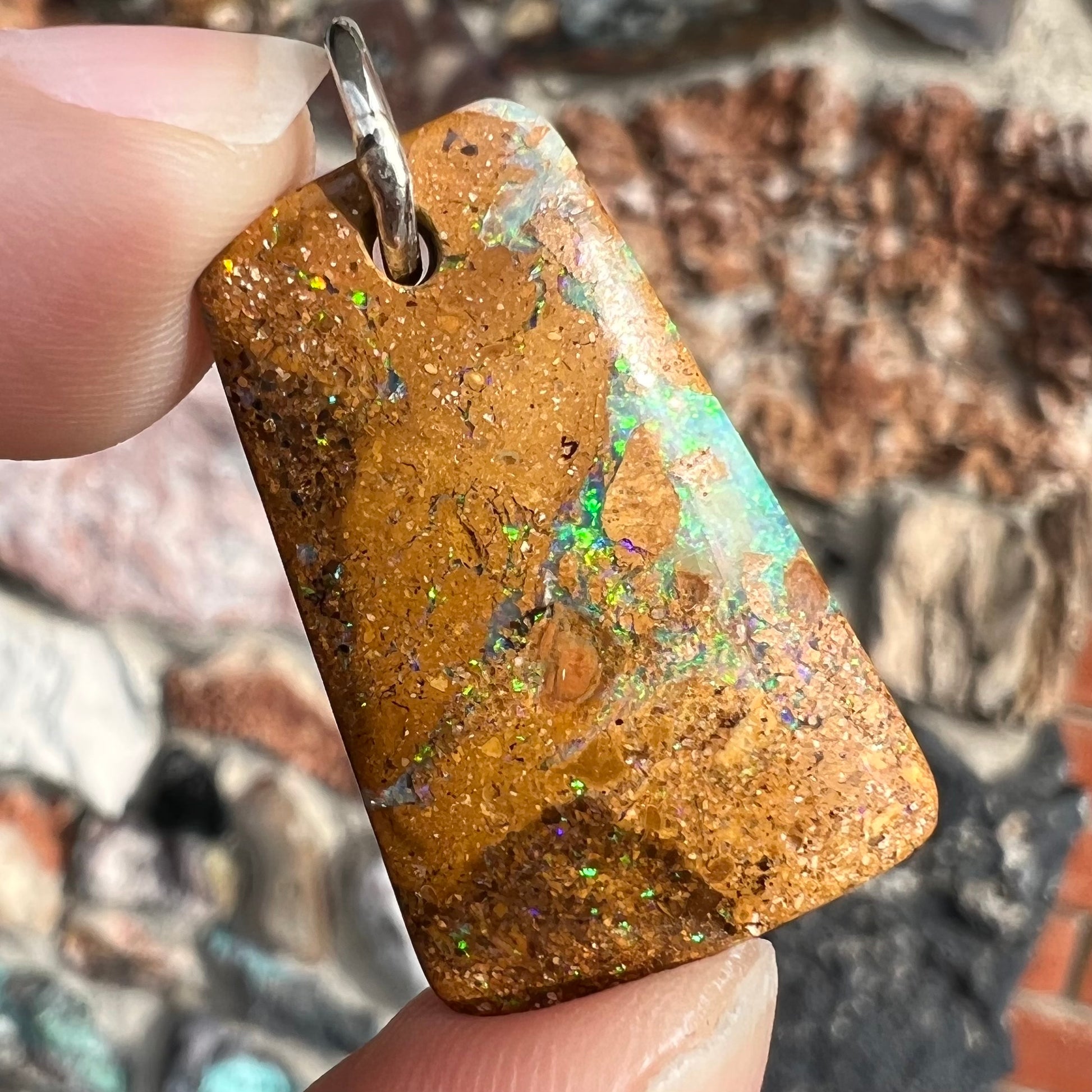 A drilled boulder opal stone with a sterling silver ring through the hole to be worn as a pendant.