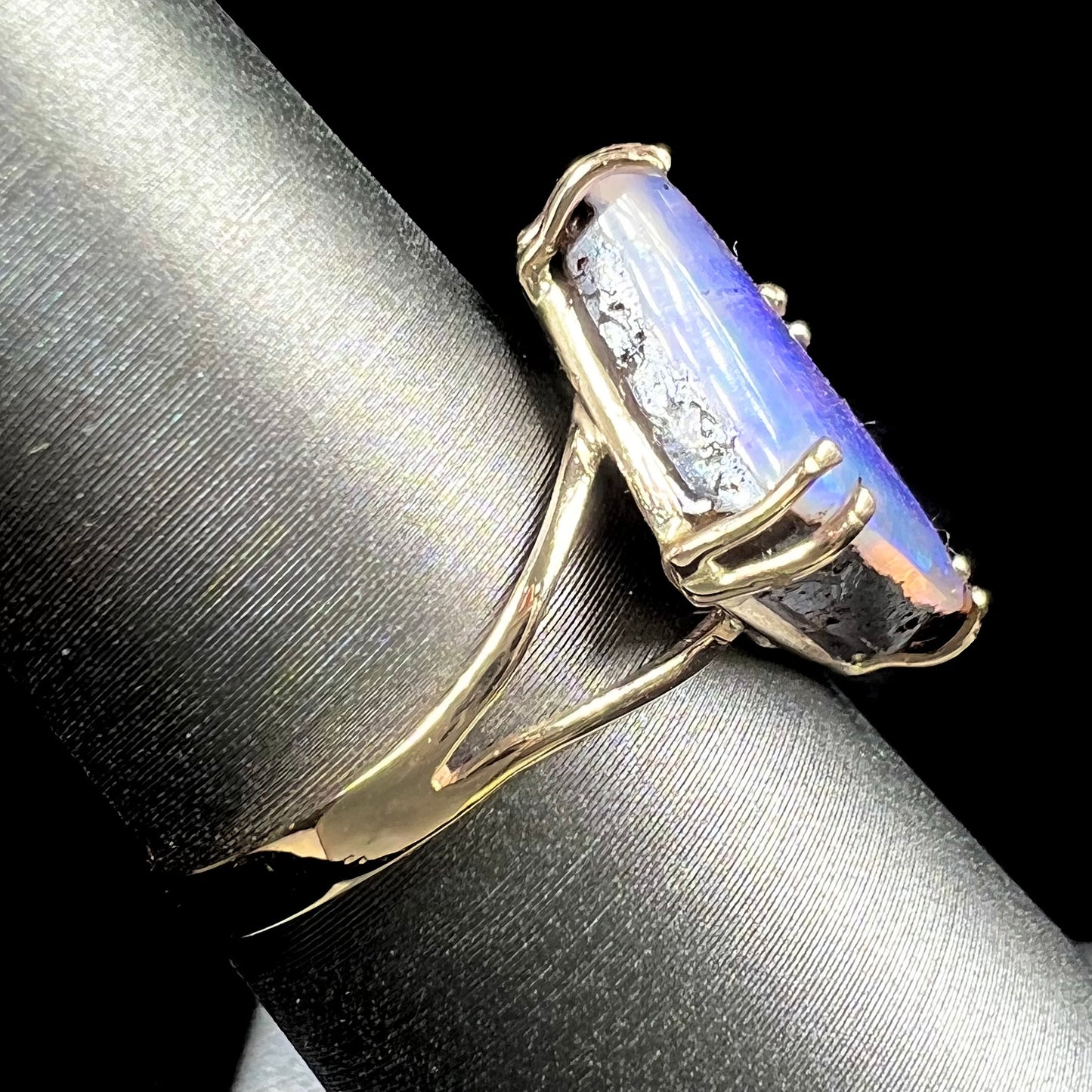 A ladies' boulder opal solitaire ring, handmade in yellow gold.  The stone is purple with flashes of blue, aqua, and green.