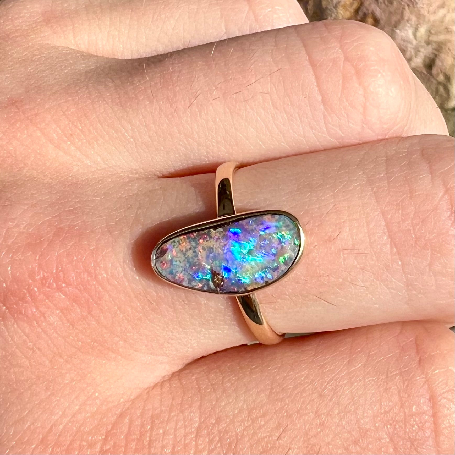 A bright, freeform cabochon cut rainbow boulder opal set in a yellow gold solitaire ring.