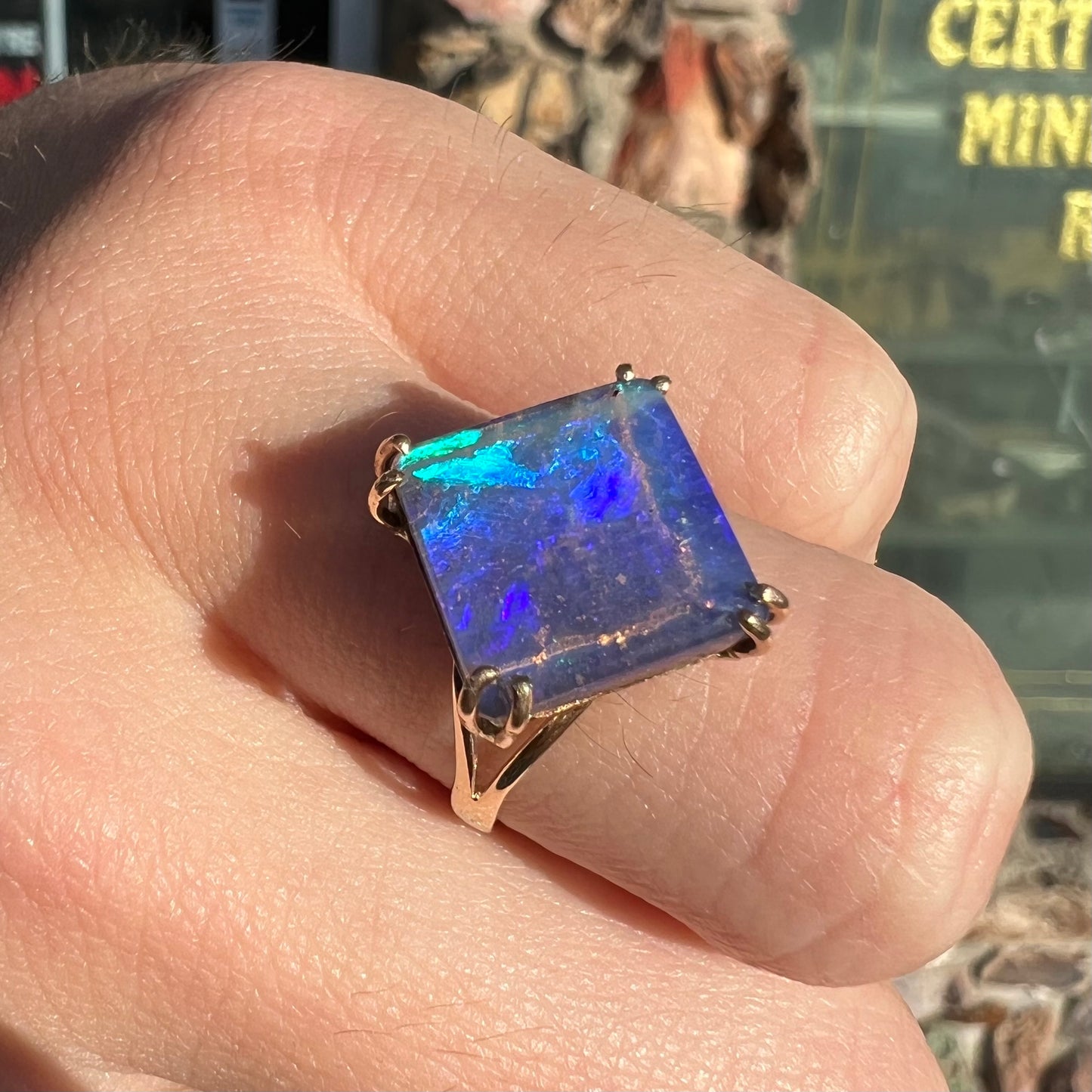 A ladies' boulder opal solitaire ring, handmade in yellow gold.  The stone is purple with flashes of blue, aqua, and green.