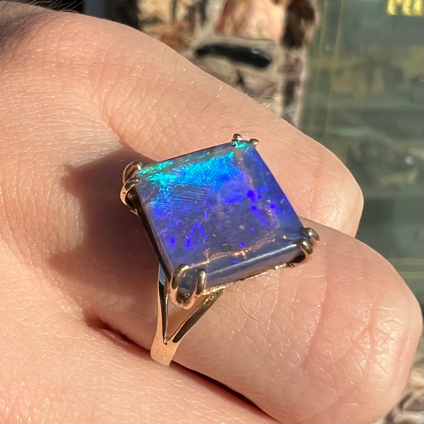 A ladies' boulder opal solitaire ring, handmade in yellow gold.  The stone is purple with flashes of blue, aqua, and green.