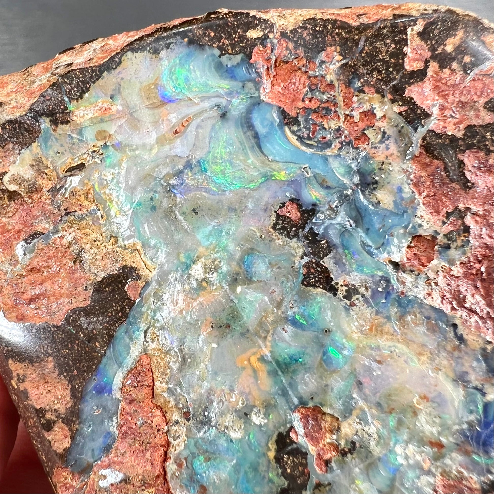 A hand-sized, polished Quilpie boulder opal specimen.  The stone shows blue, green, and orange flashes.