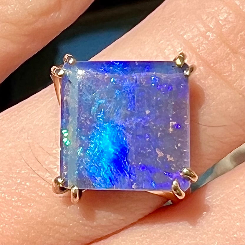 A ladies' boulder opal solitaire ring, handmade in yellow gold.  The stone is purple with flashes of blue, aqua, and green.