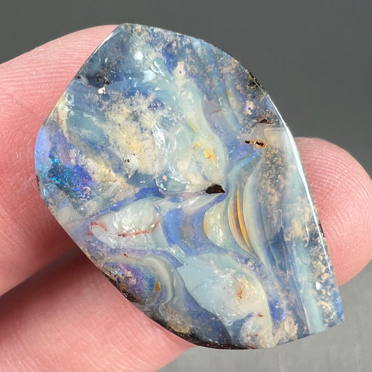 A loose, polished, freeform cut boulder opal stone from Queensland, Australia.