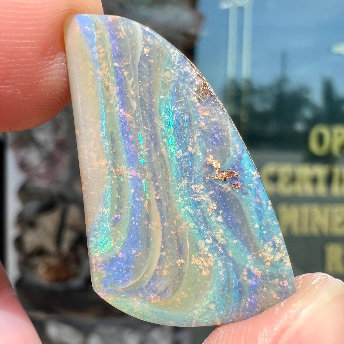 A polished, freeform shaped boulder opal stone from Queensland, Australia.  Predominant colors are green, blue, and violet.