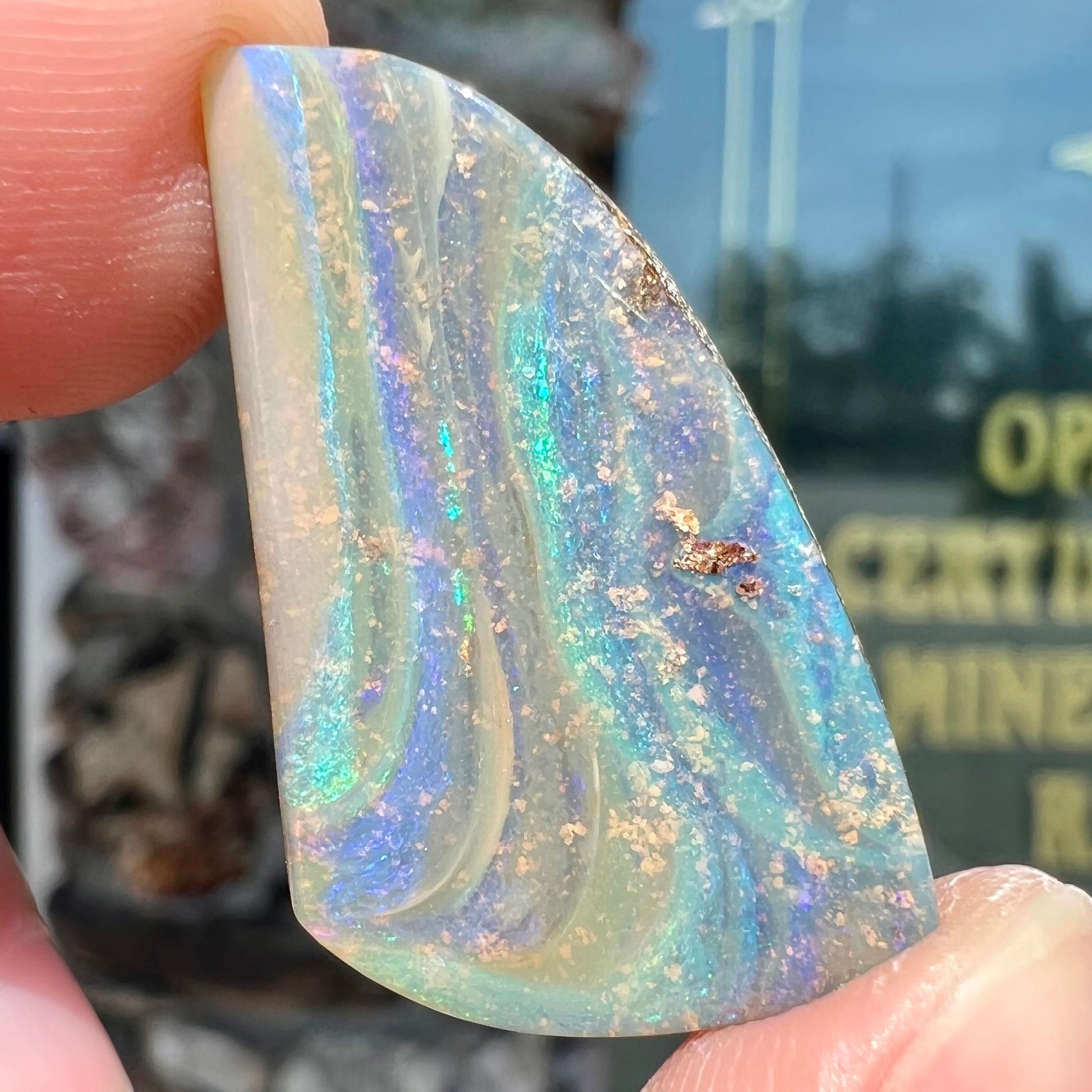 A polished, freeform shaped boulder opal stone from Queensland, Australia.  Predominant colors are green, blue, and violet.