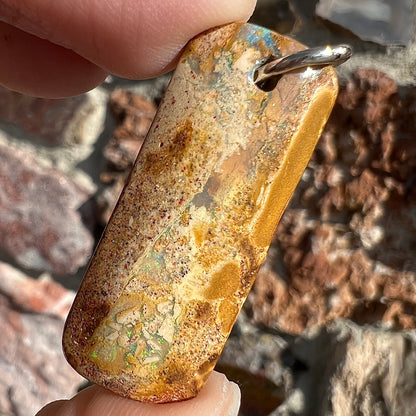 A drilled boulder opal stone with a sterling silver ring through the hole to be worn as a pendant.