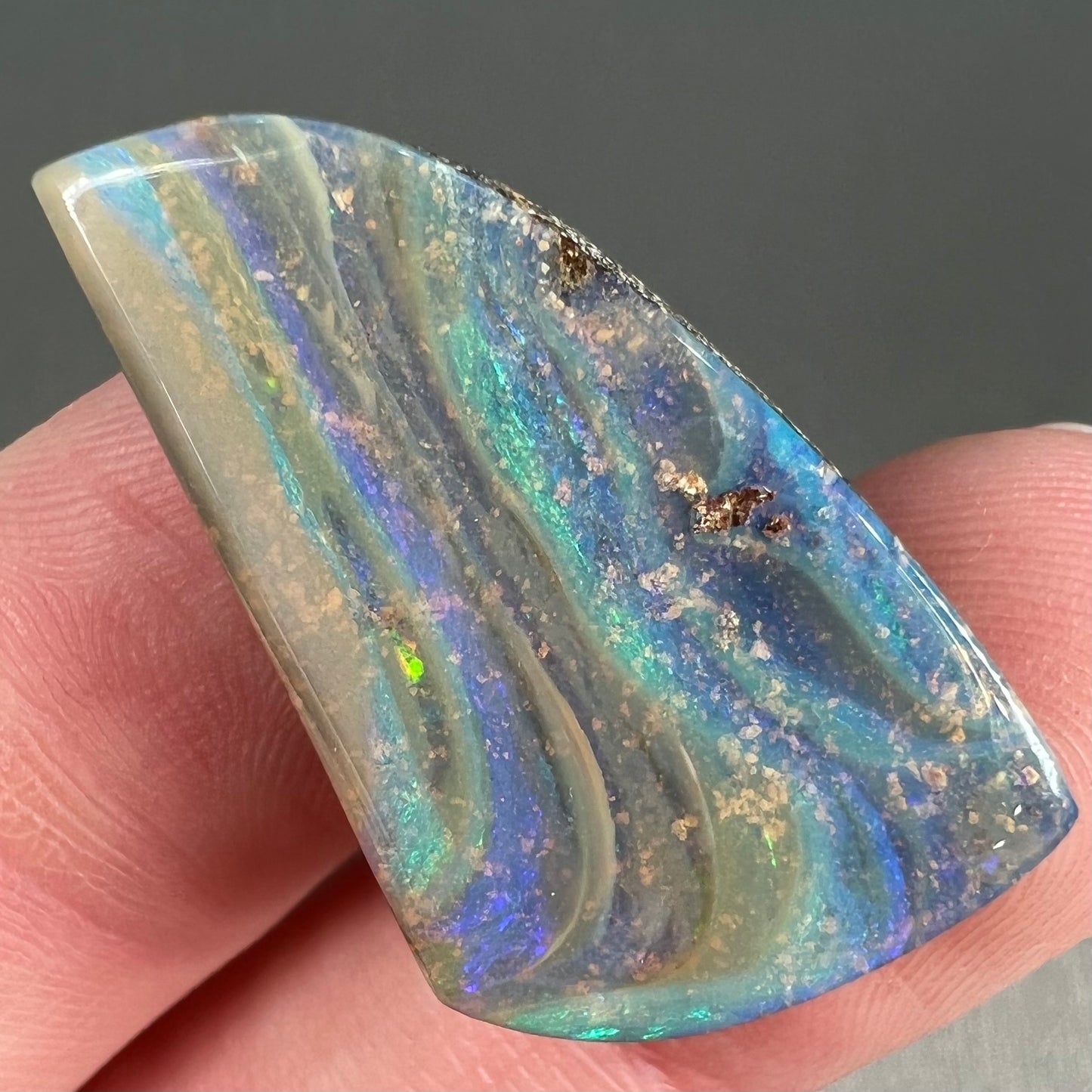 A polished, freeform shaped boulder opal stone from Queensland, Australia.  Predominant colors are green, blue, and violet.