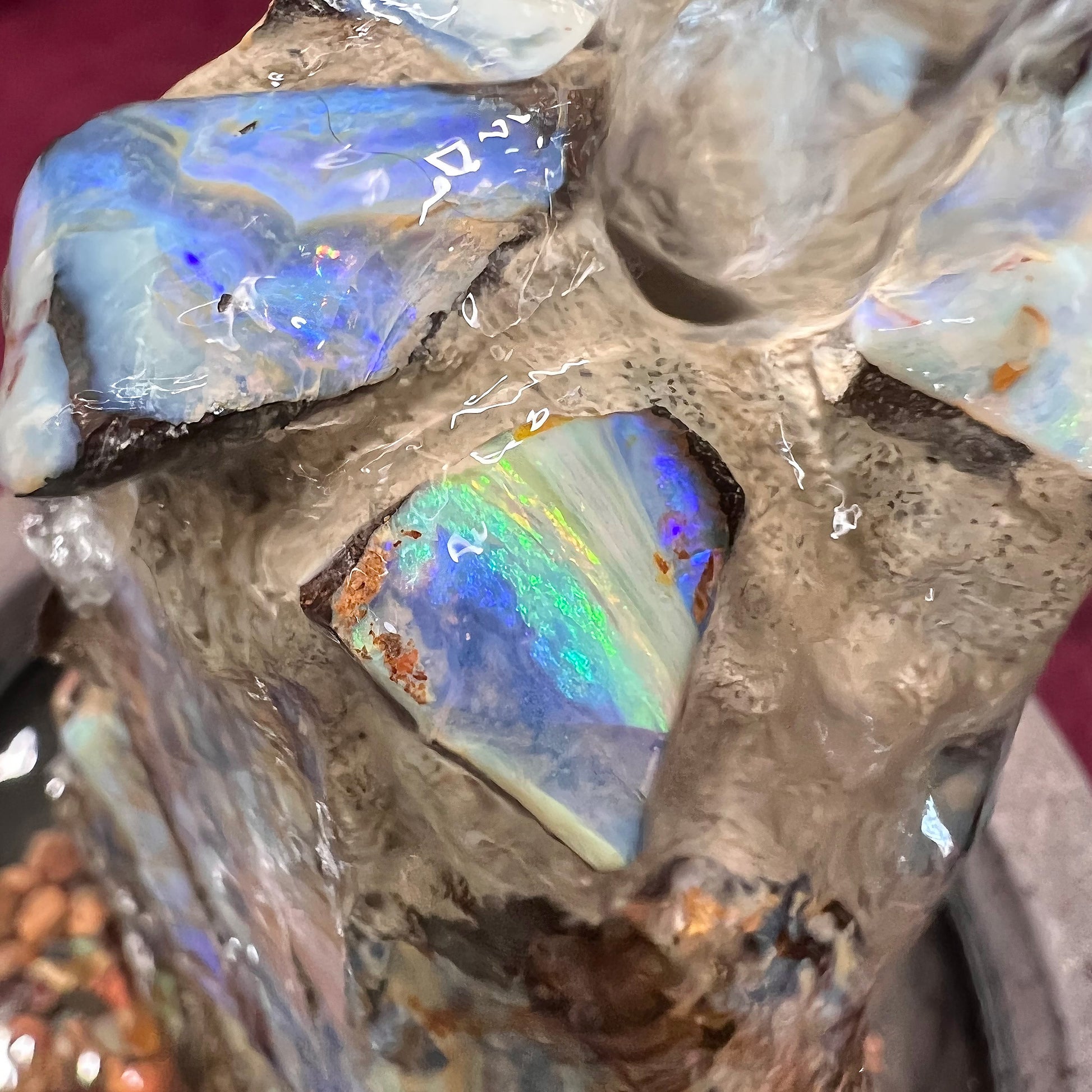 An indoor/outdoor three sided pyramid fountain made from Australian boulder opal, sitting in a bowl of Mexican fire opal.