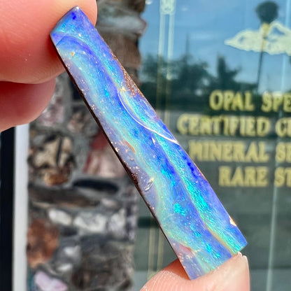 A loose, polished, wedge shaped boulder opal stone from Queensland, Australia.