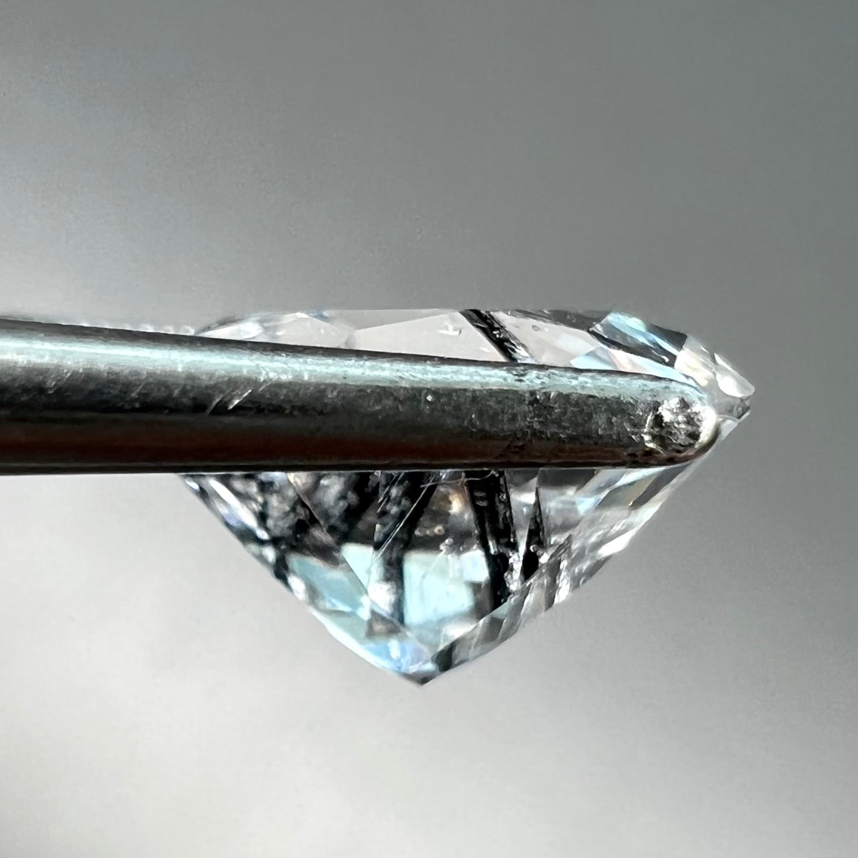 A round brilliant cut clear quartz stone with two black tourmaline crystal inclusions.