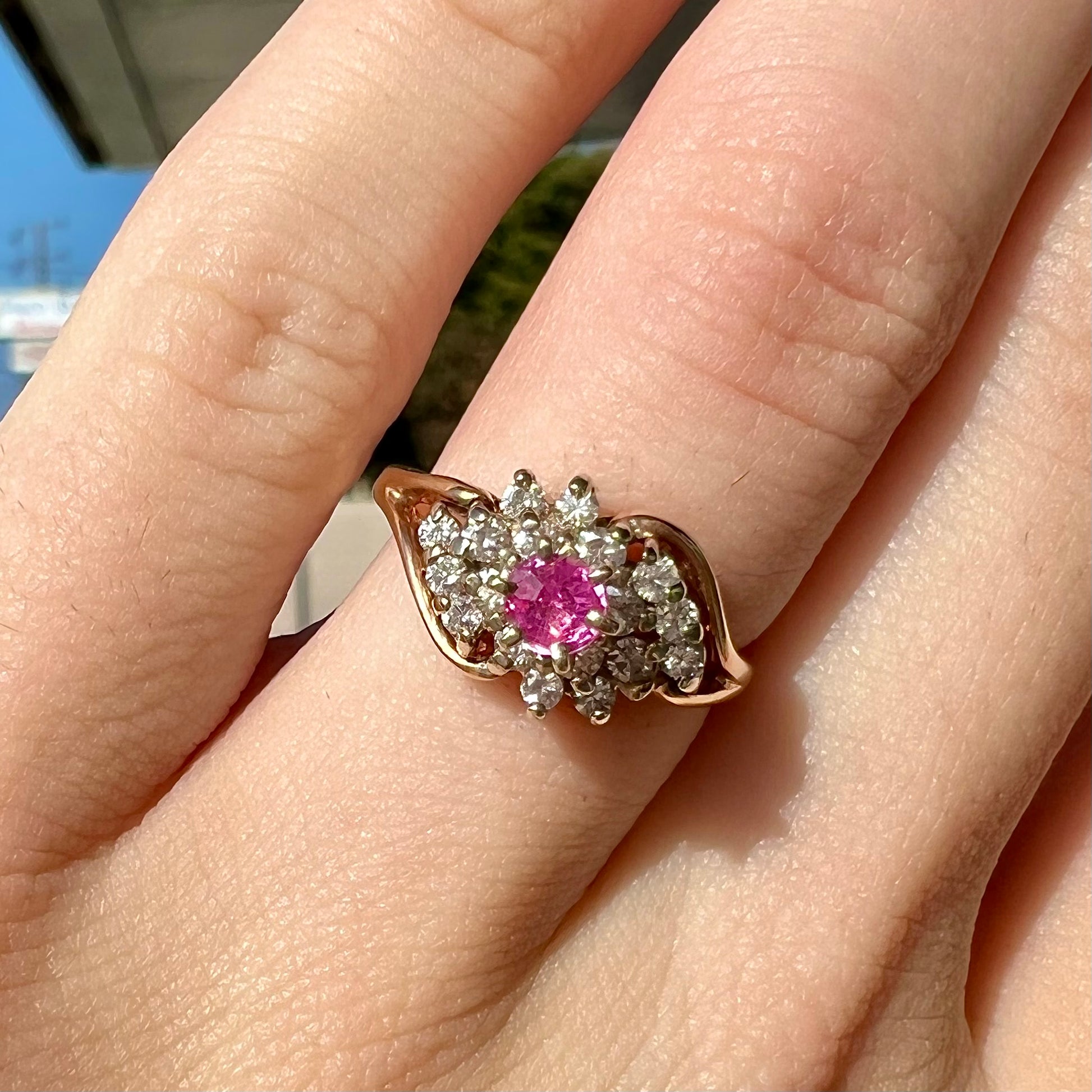 A round pink sapphire high-set in a yellow gold diamond cluster ring.