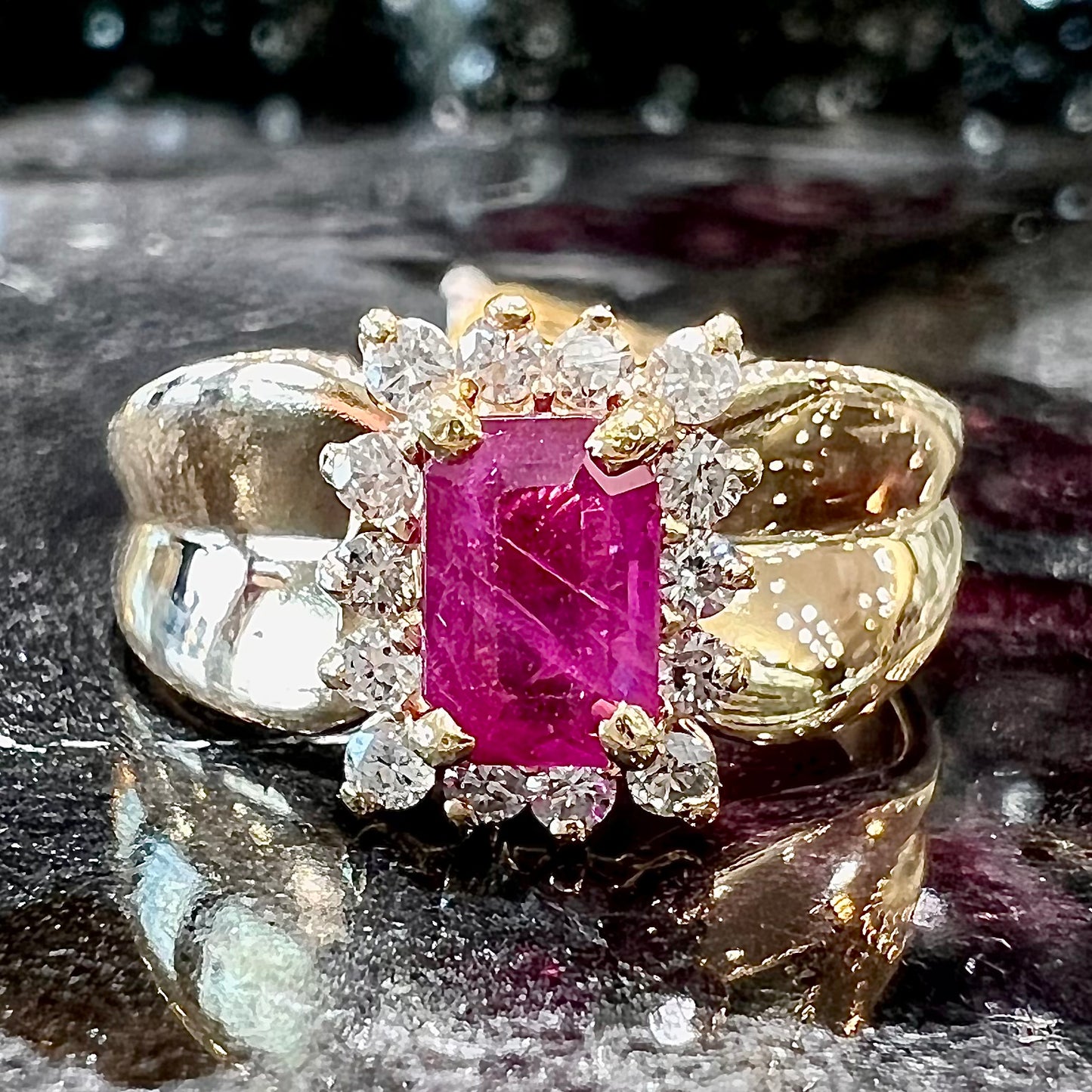 A yellow gold ring set with an emerald cut red ruby surrounded by a halo of round diamonds.