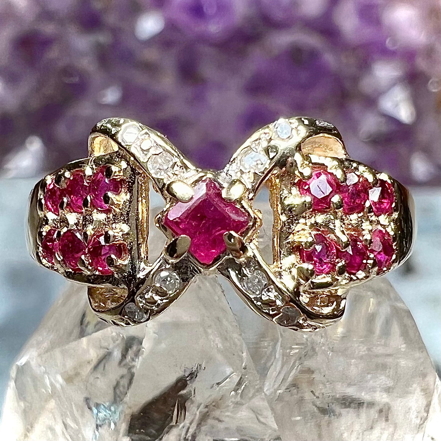 A yellow gold princess cut ruby ring set with round ruby and diamond accents.