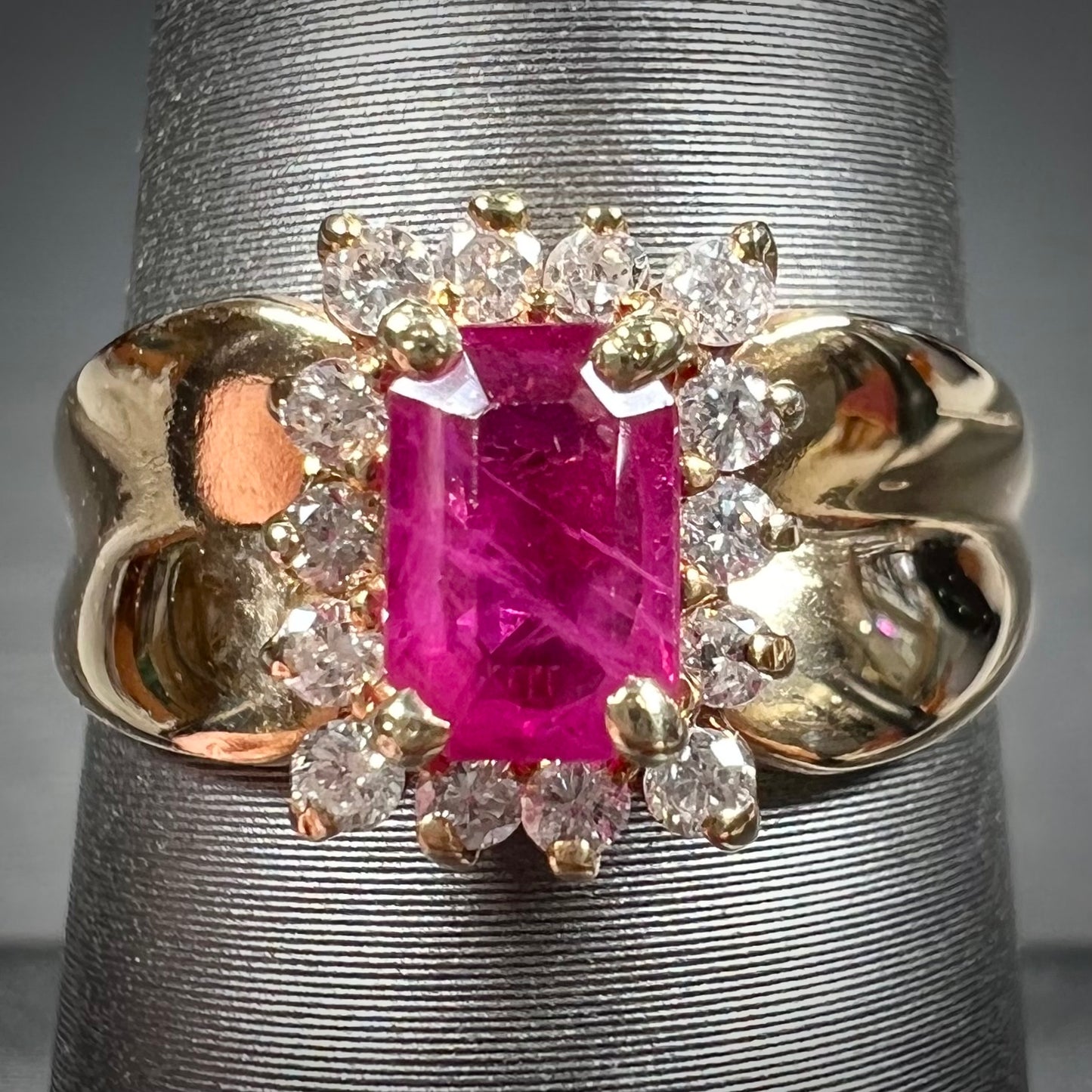 A yellow gold ring set with an emerald cut red ruby surrounded by a halo of round diamonds.