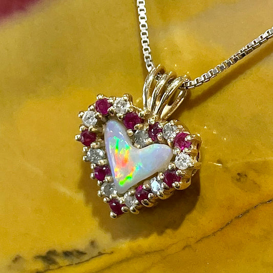 A yellow gold pendant set with a heart cut white opal in a halo of alternating round rubies and diamonds.
