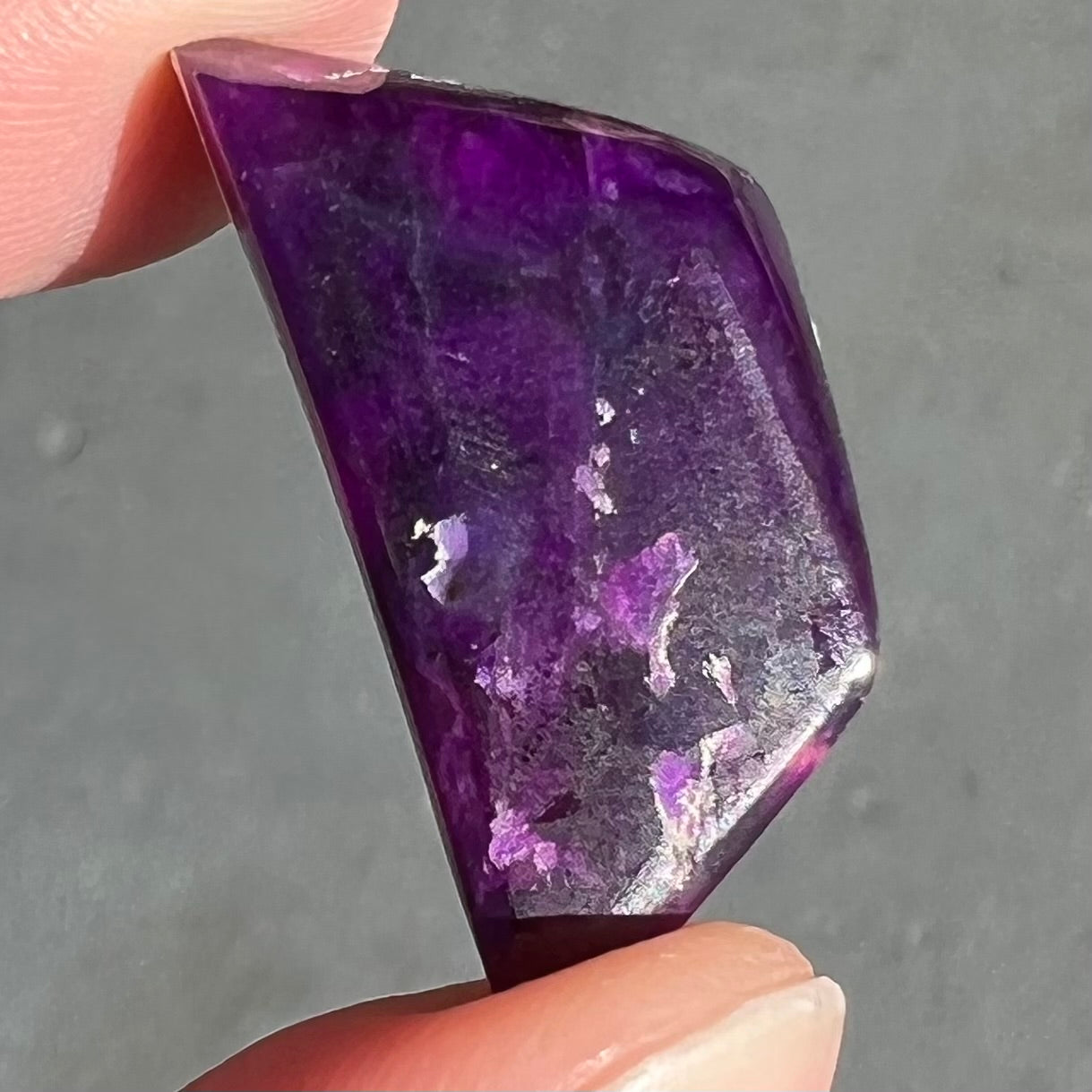 A freeform cabochon cut piece of dark purple sugilite.