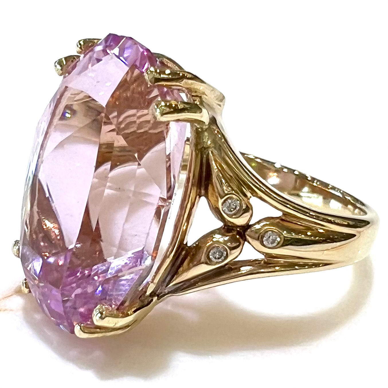 A large, pink kunzite is prong set into a 14kt yellow gold basket-style ring mounting with three diamonds flush set into the design on each side.