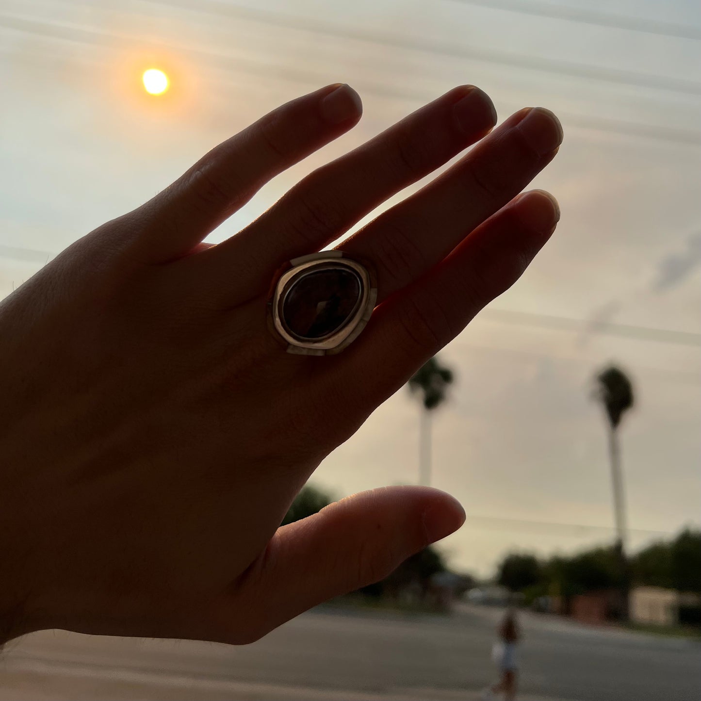 A hand wearing a petrified wood ring covering the smoke covered sun in Orange County, California.