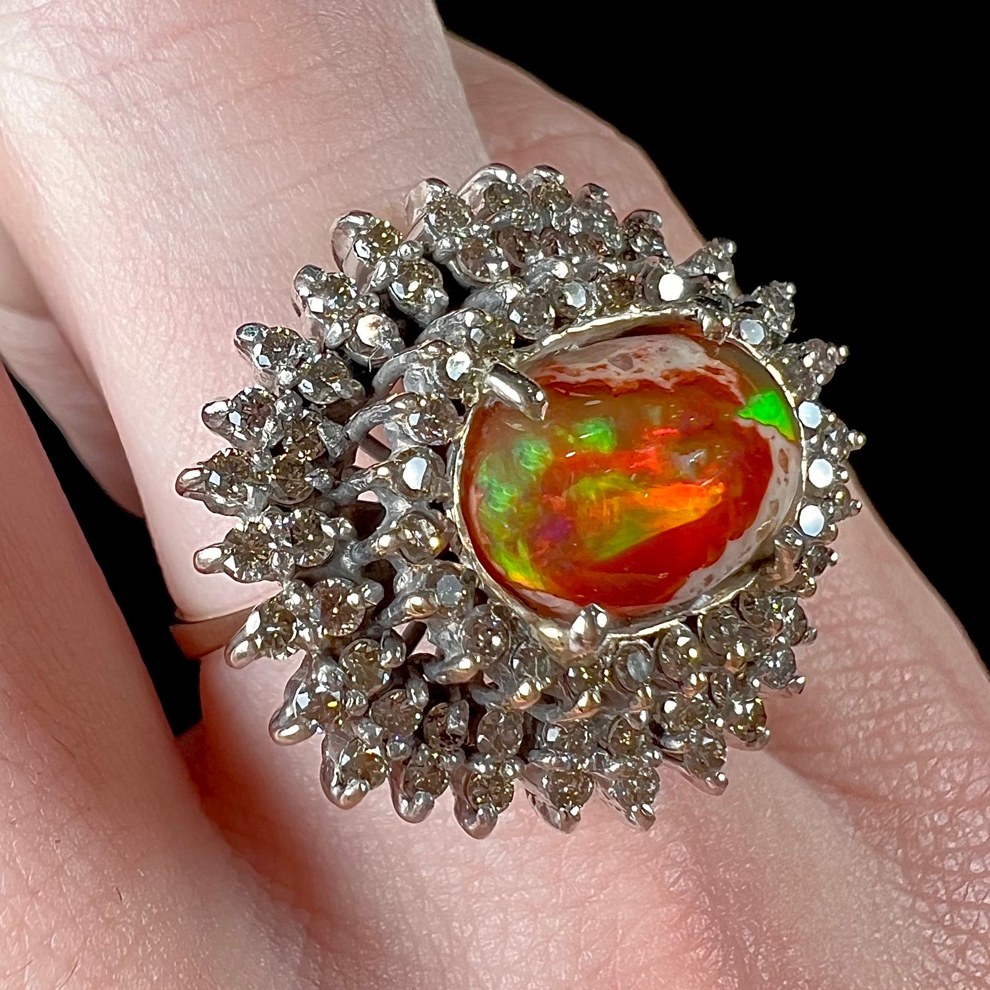 An 18k white gold orange fire opal ring set with a triple halo of diamonds.