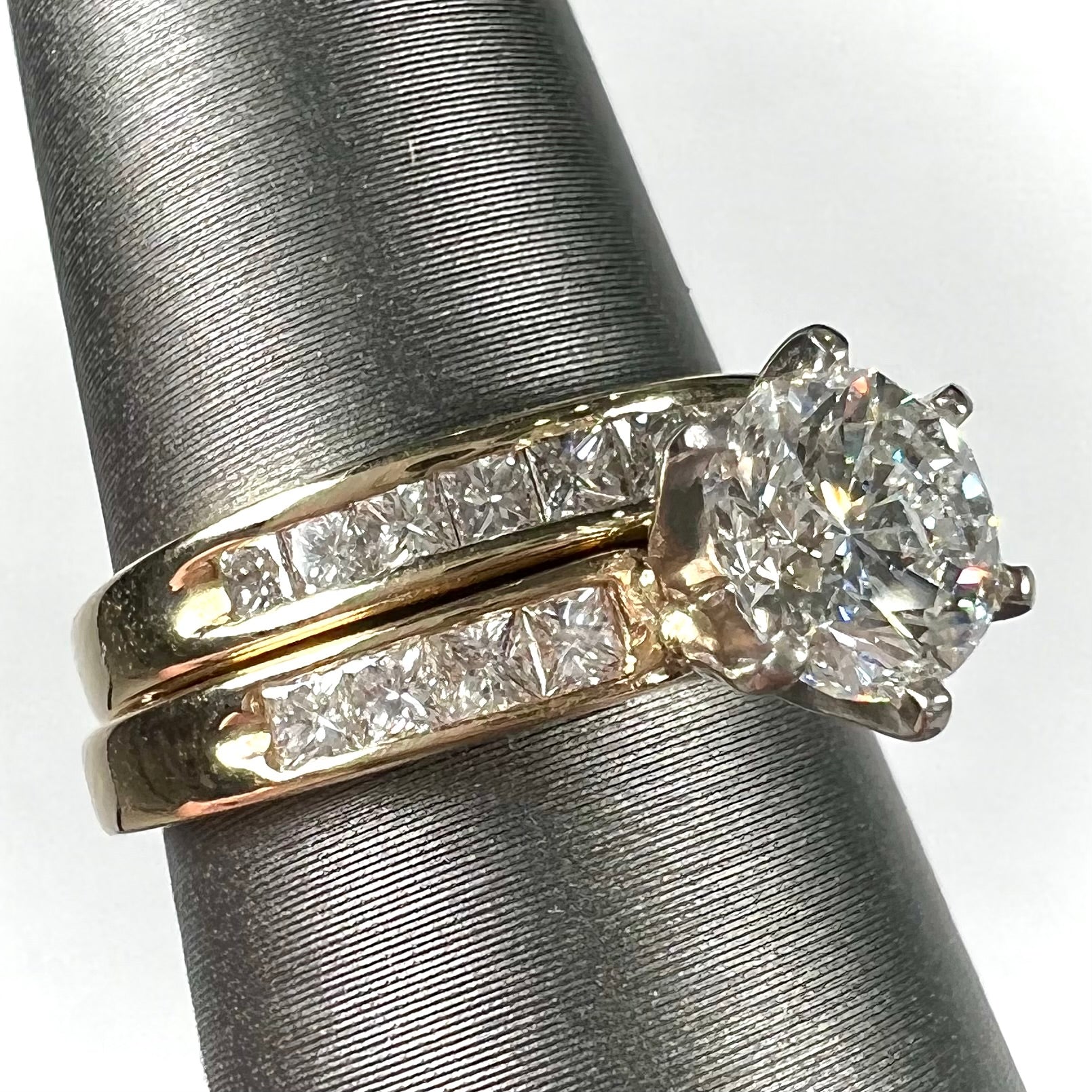 A diamond engagement and wedding ring set.  The center stone is a 1 carat round diamond, and the side stones are channel set princess cut diamonds.