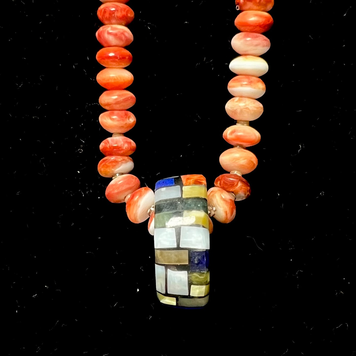 A handmade seashell pendant inlaid with spiny oyster, mother of pearl, and lapis lazuli on a spiny oyster bead necklace by Charlene Reano.