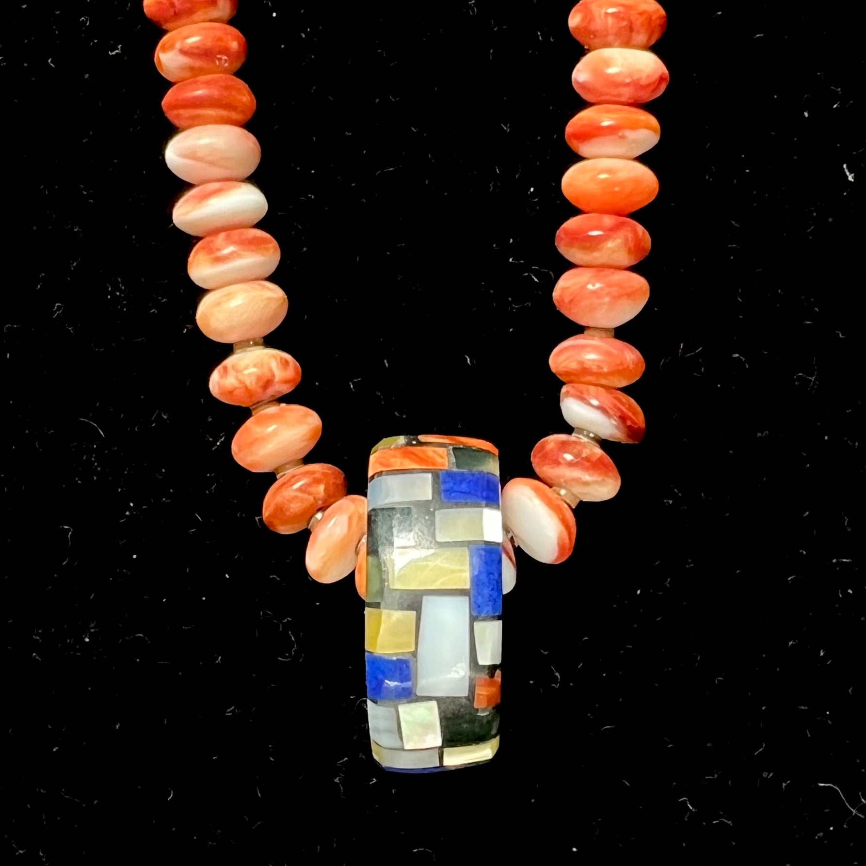 A handmade seashell pendant inlaid with spiny oyster, mother of pearl, and lapis lazuli on a spiny oyster bead necklace by Charlene Reano.
