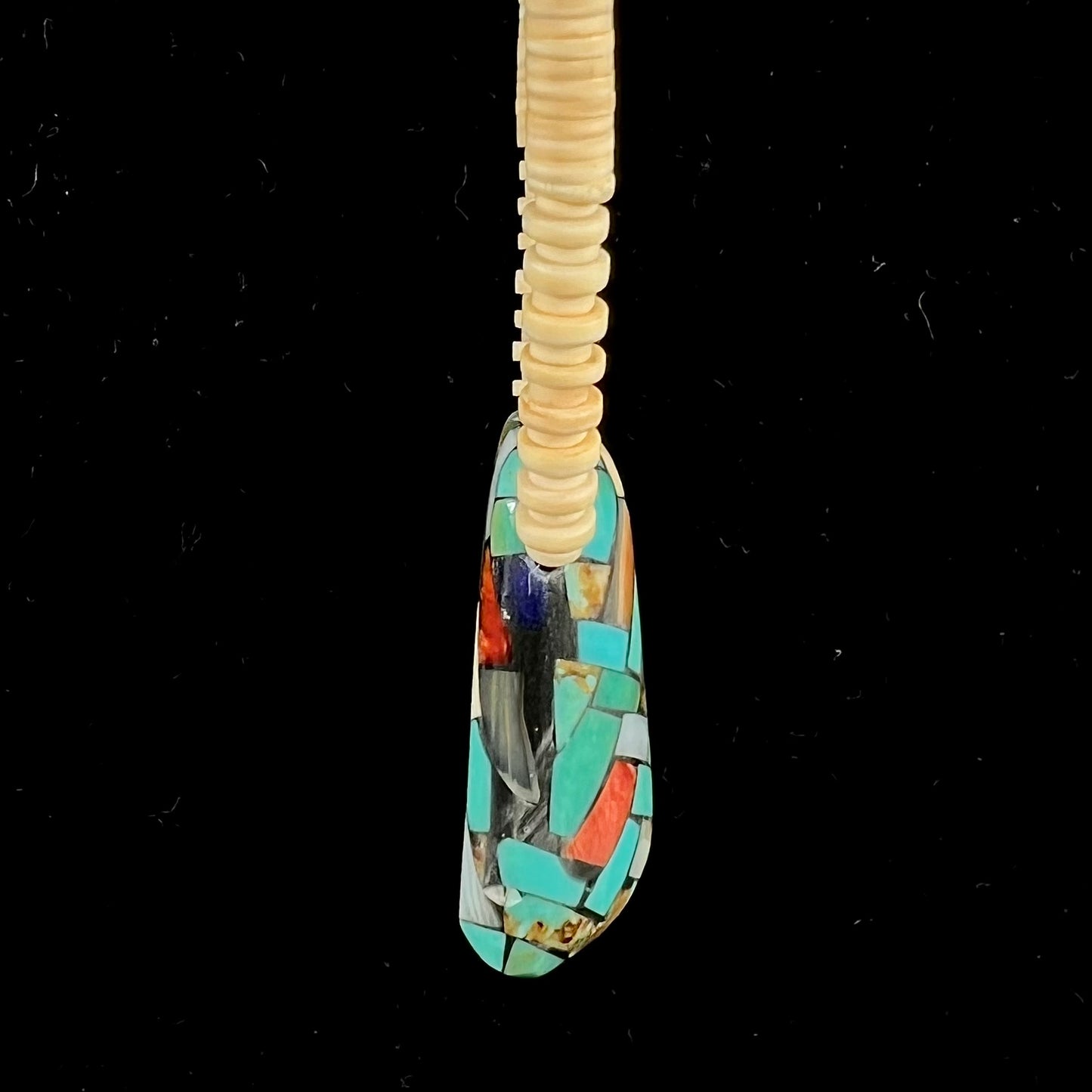 A three dimensional mosaic stone inlay pendant set with turquoise, lapis lazuli, coral, and mother of pearl on a puka shell necklace.