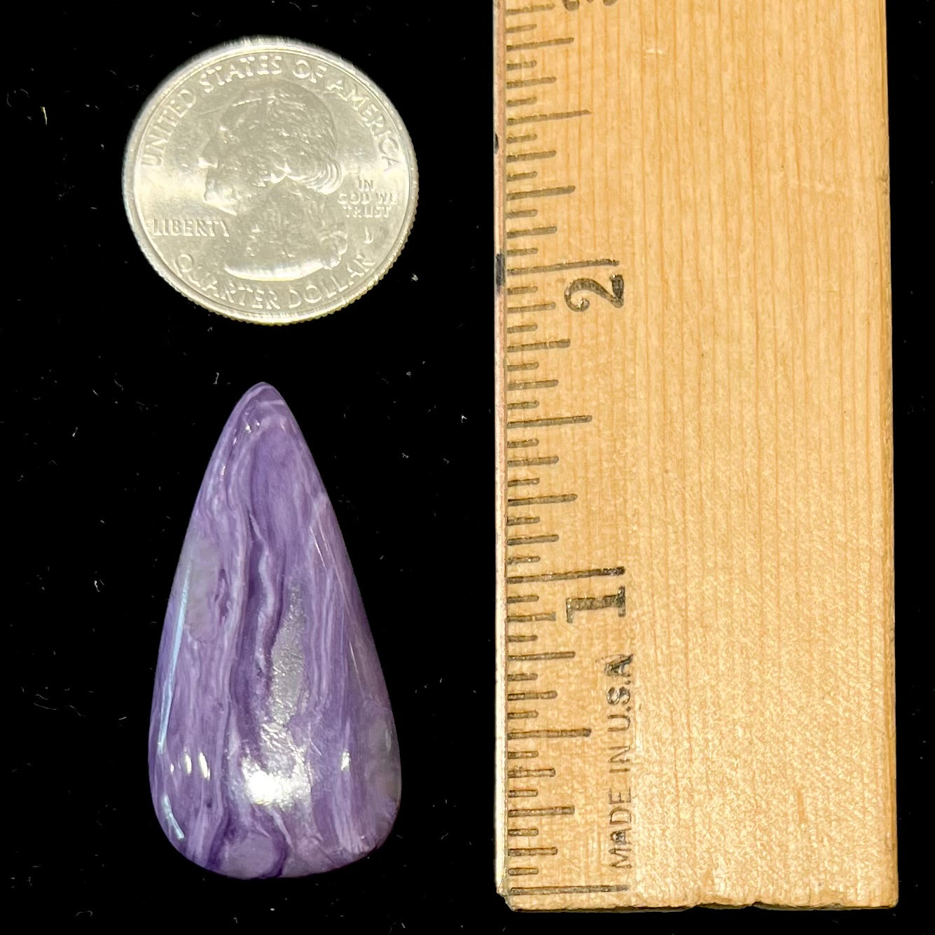 A pear shaped cabochon cut purple charoite stone.