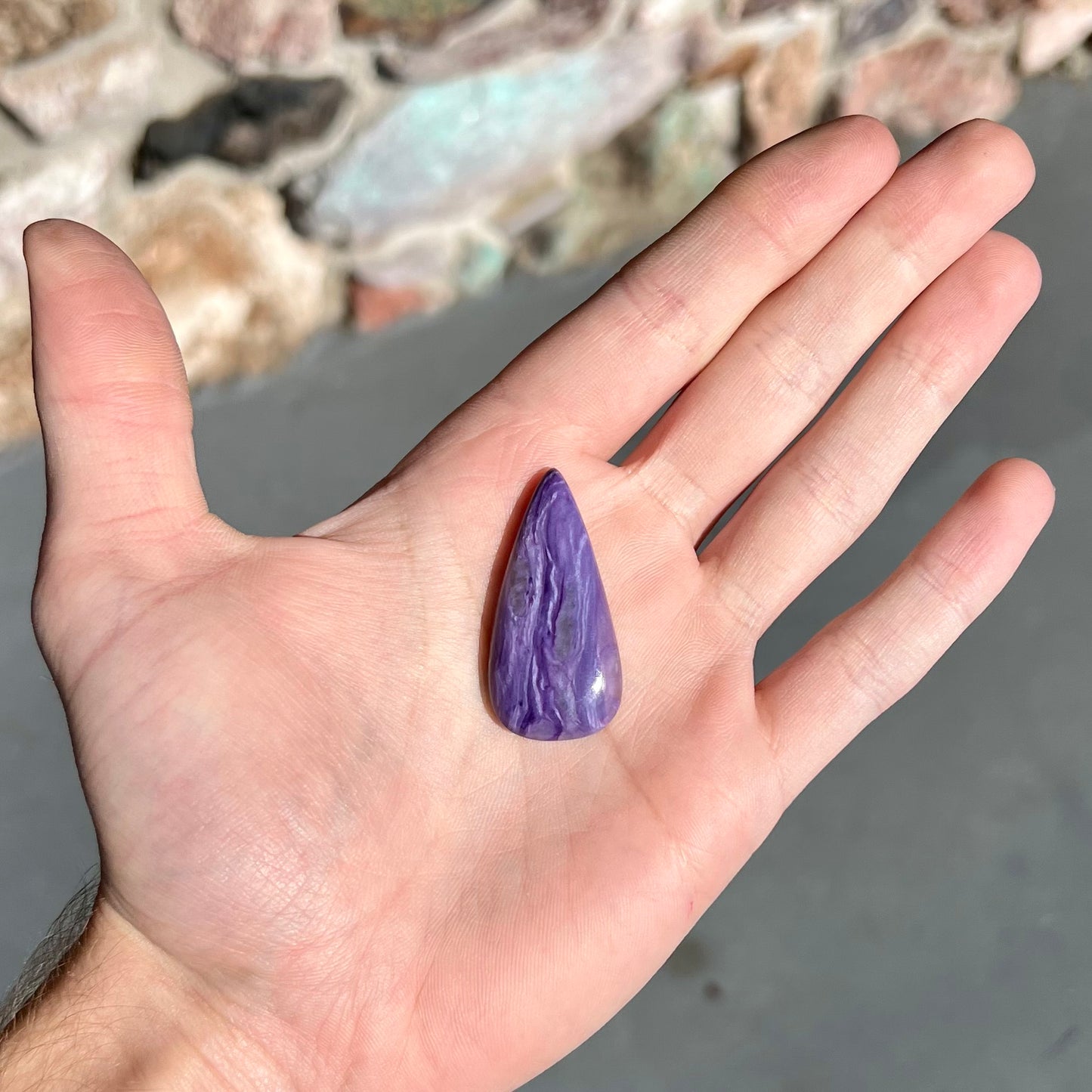 A pear shaped cabochon cut purple charoite stone.