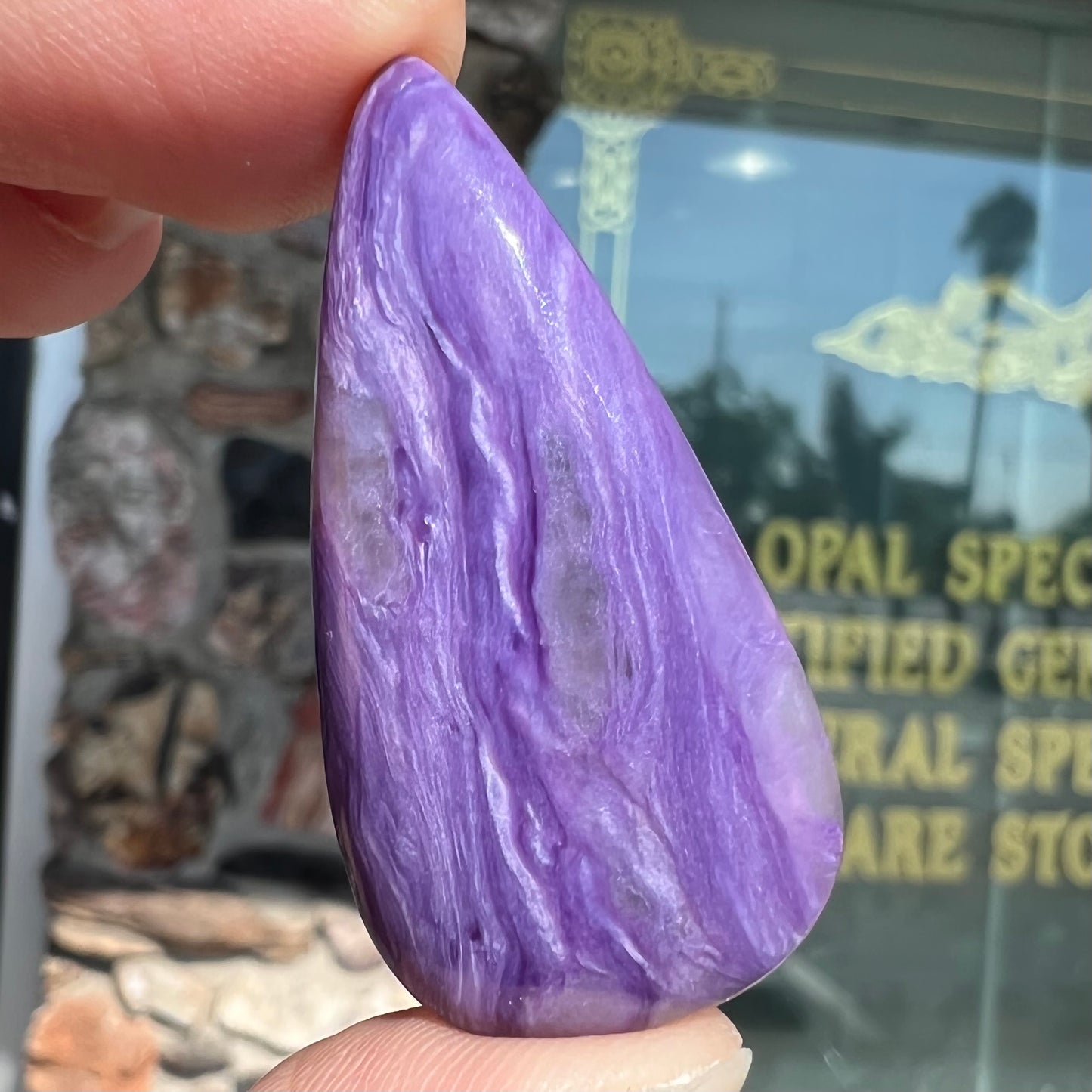 A pear shaped cabochon cut purple charoite stone.